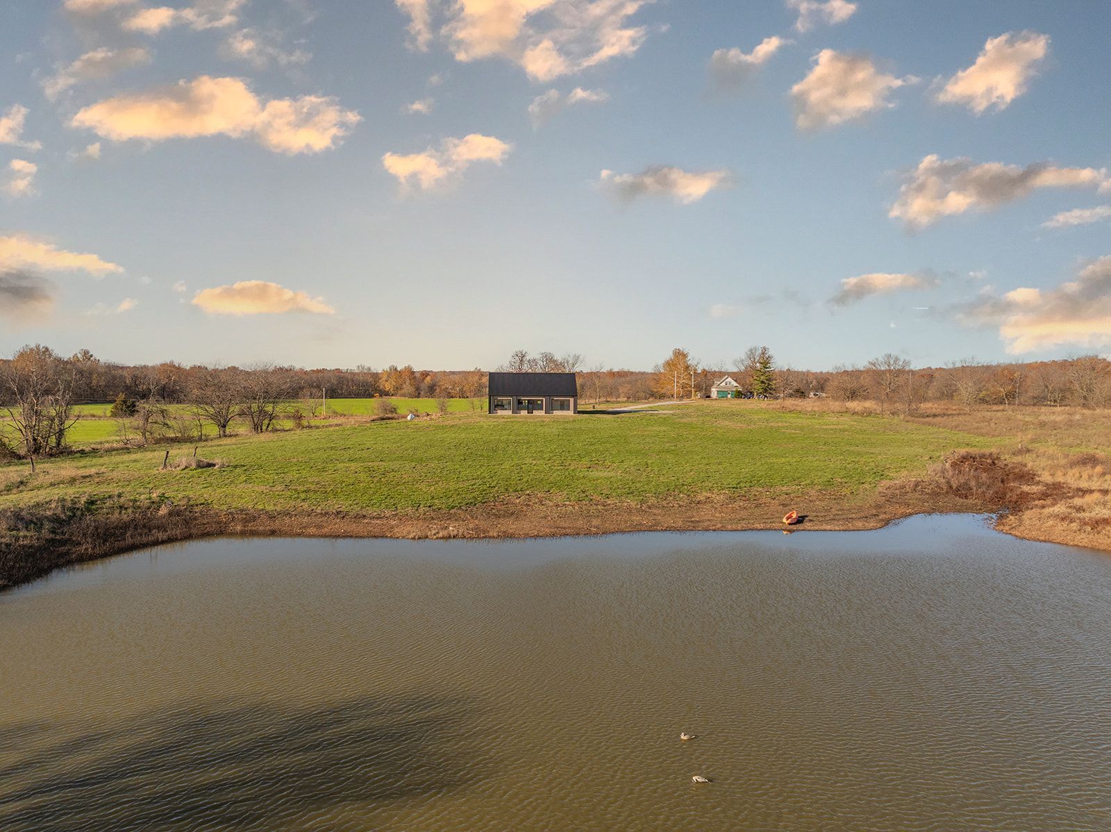 A small pond in the middle of a field with a barn in the background.