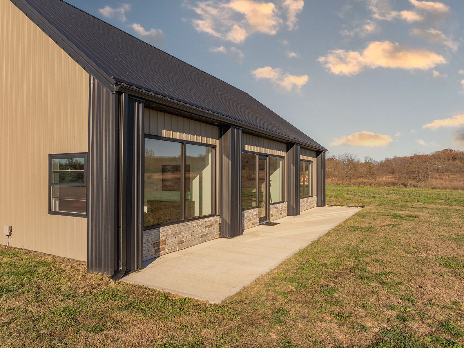 A small house with a black roof is sitting in the middle of a grassy field.