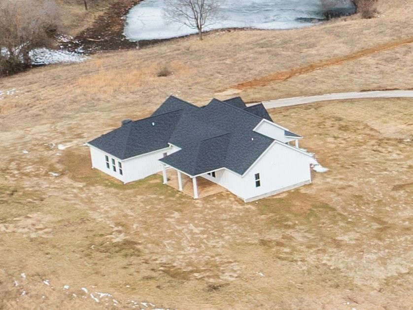 An aerial view of a house in a field with a pond in the background.