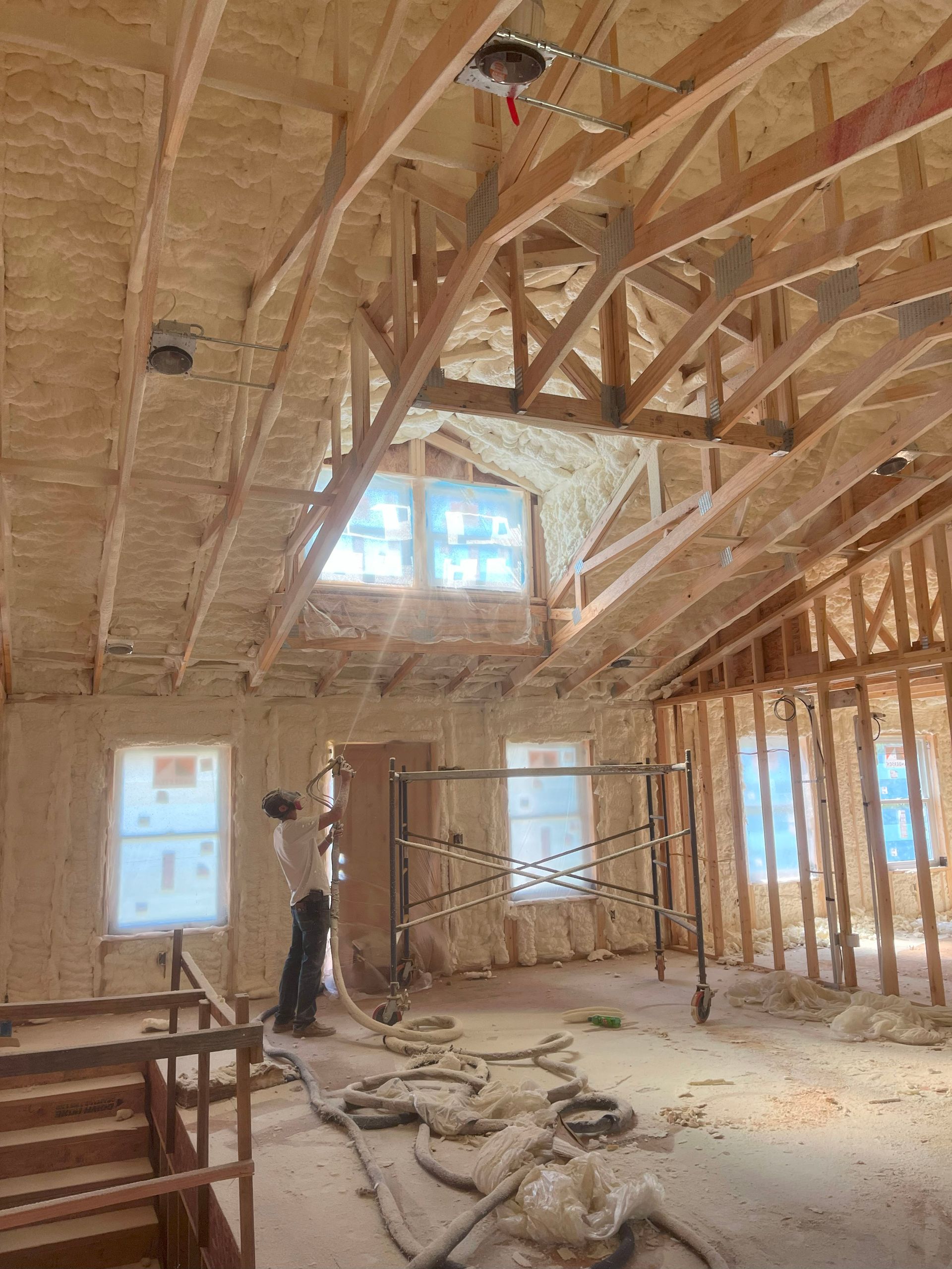 A man is spraying insulation on the ceiling of a building under construction.