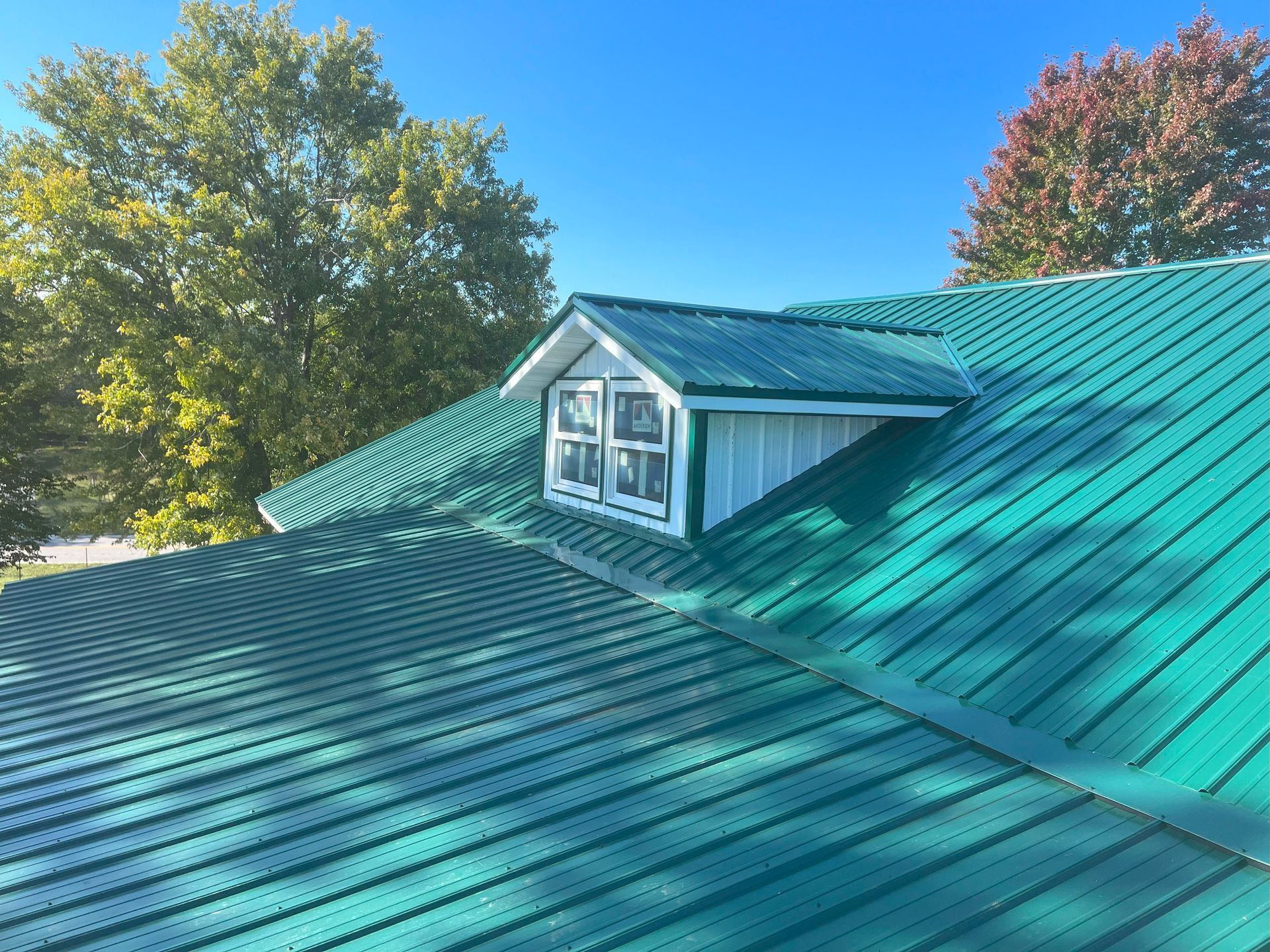 A green roof with a window on it and trees in the background.