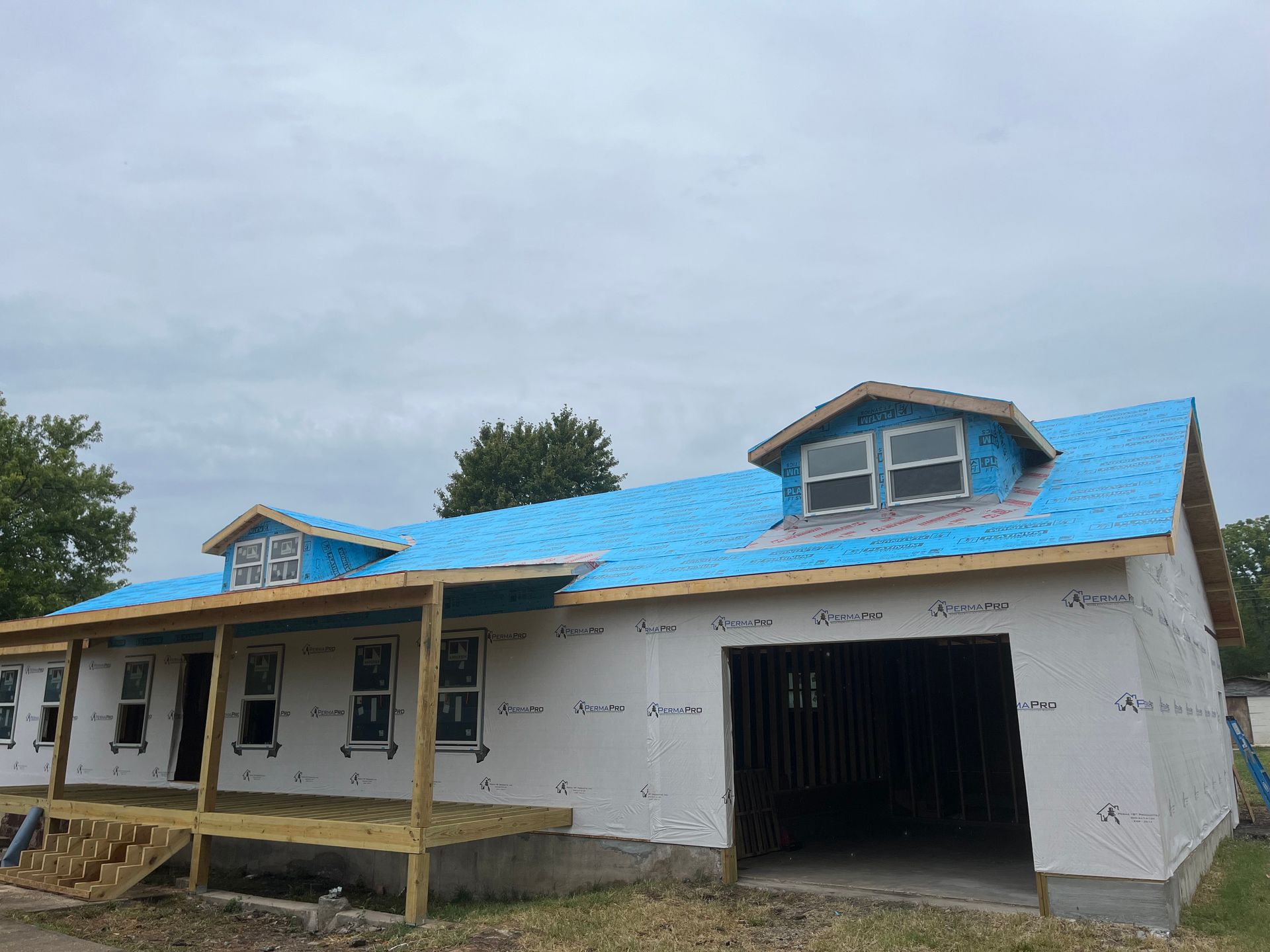 A house under construction with a blue roof and a porch.