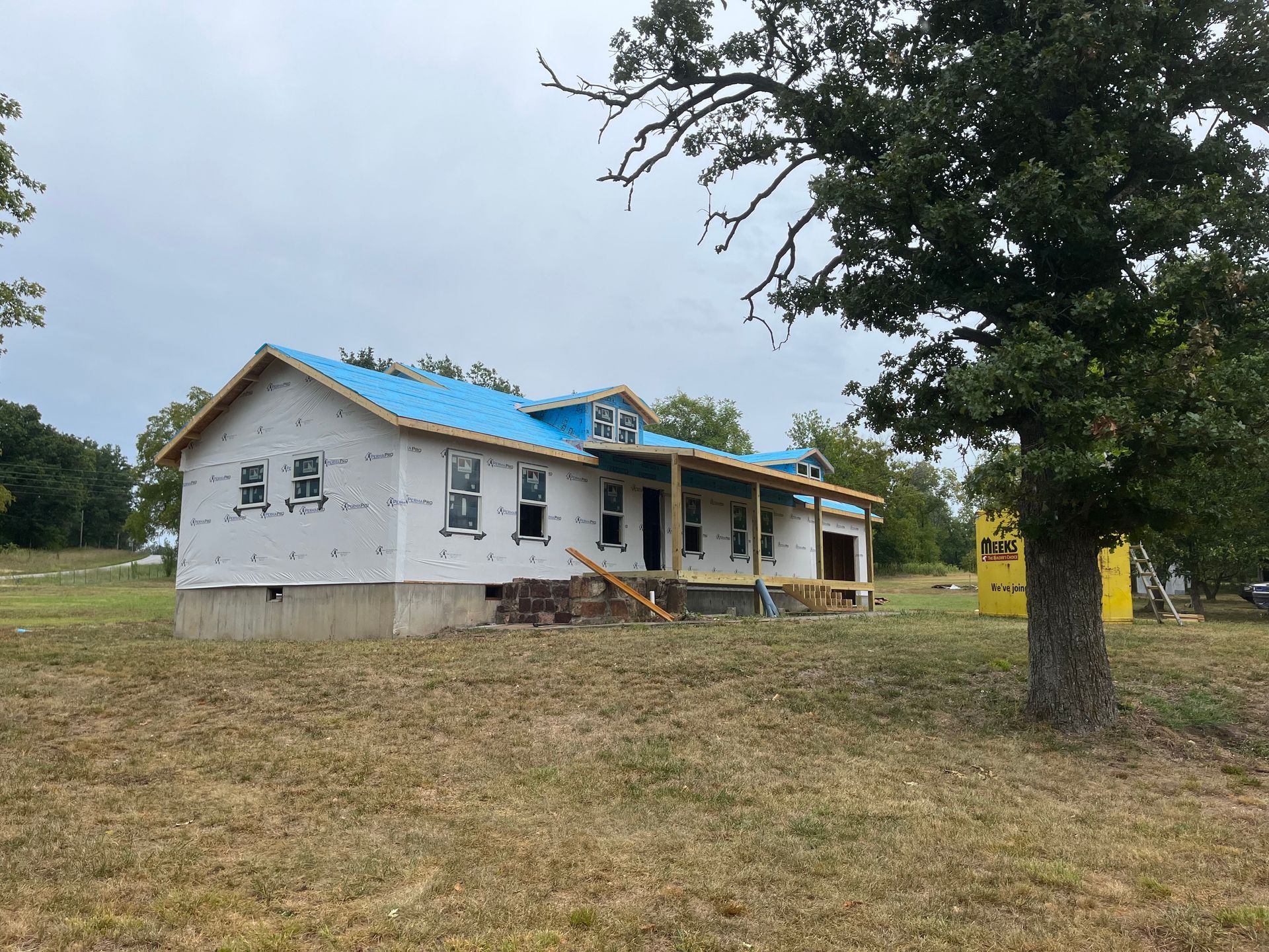 A house is being built in a field with a tree in the foreground.