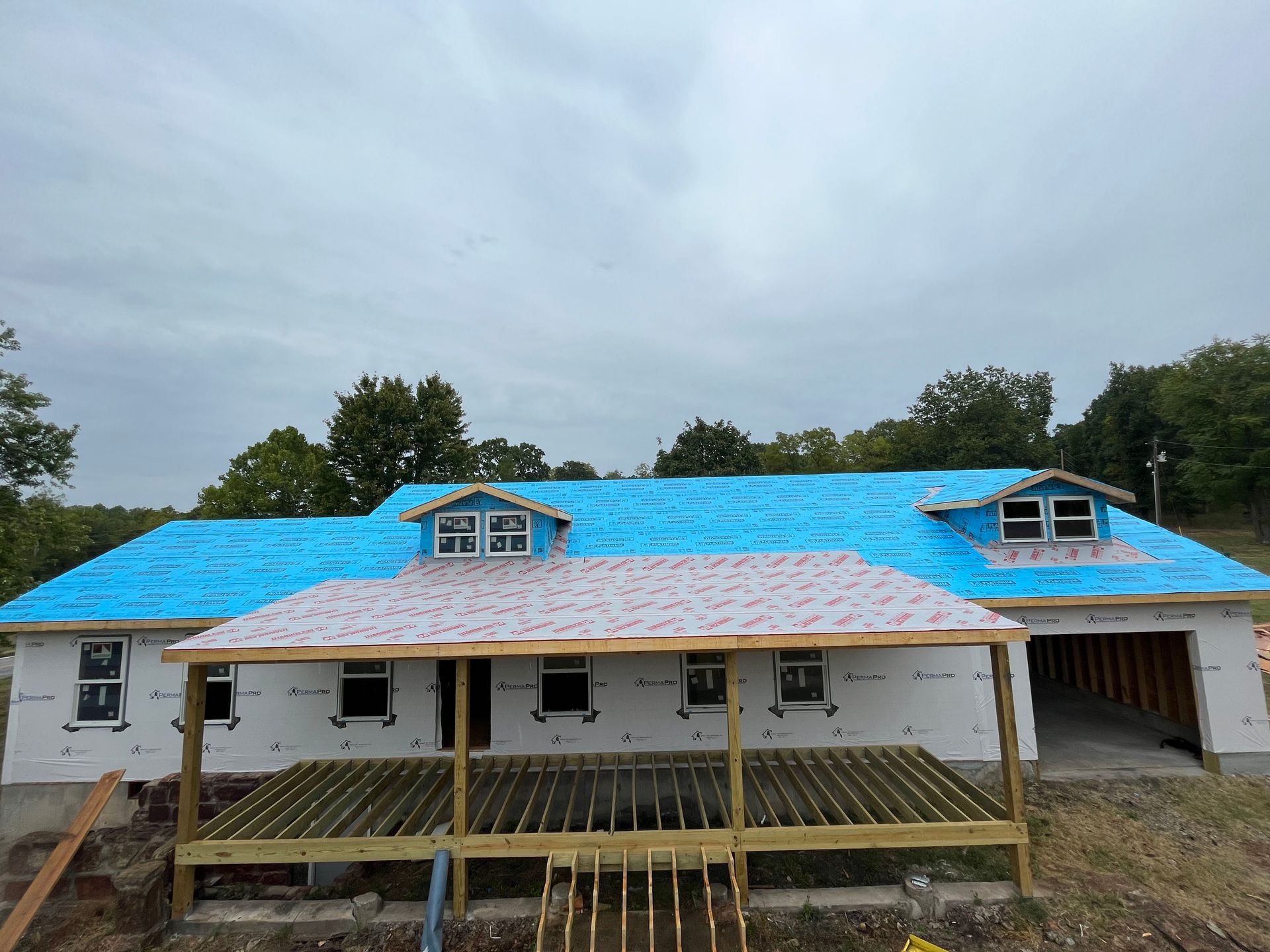 A house under construction with a blue roof and a porch.