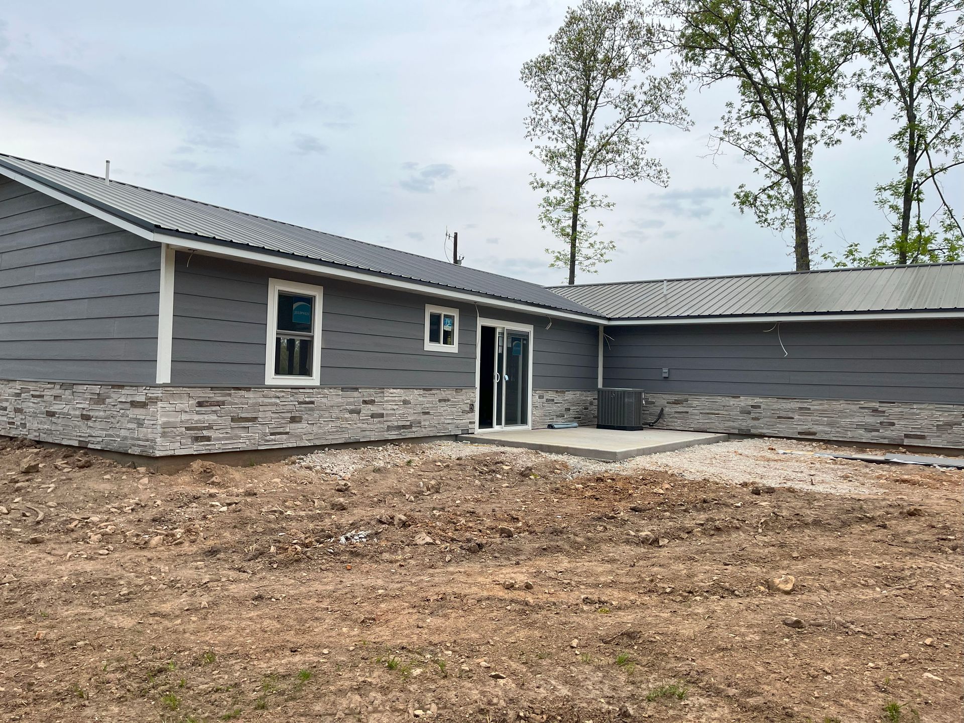 A large gray house is sitting in the middle of a dirt field.
