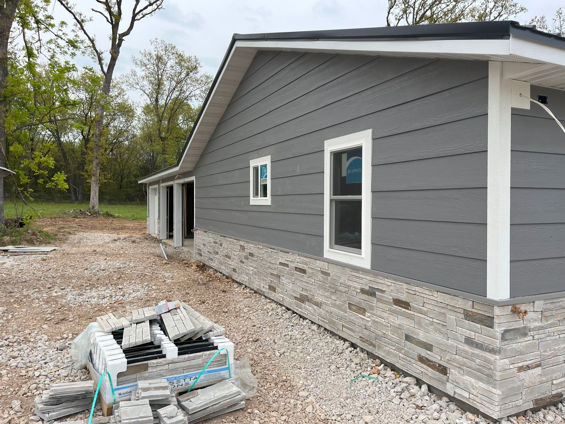 A gray house is being built on a gravel lot.
