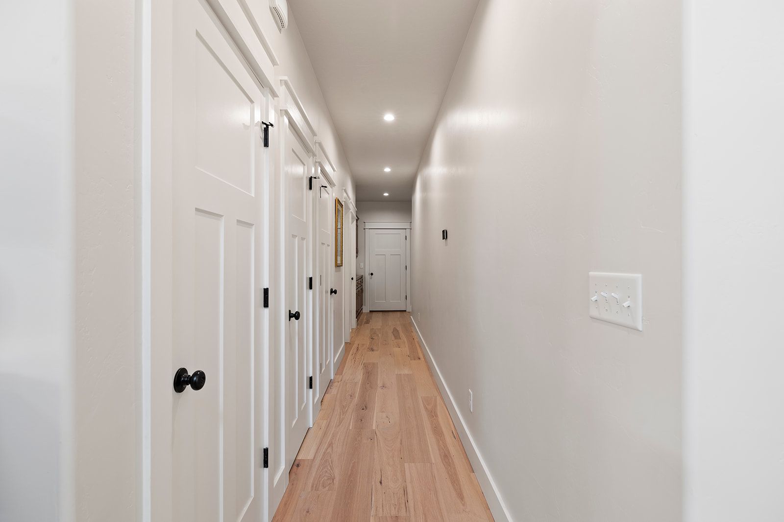 A long hallway with white walls and hardwood floors in a house.