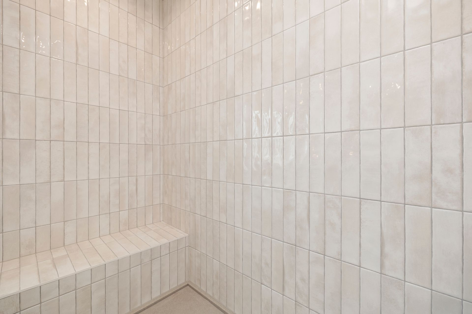 A shower with white tiles and a bench in it.