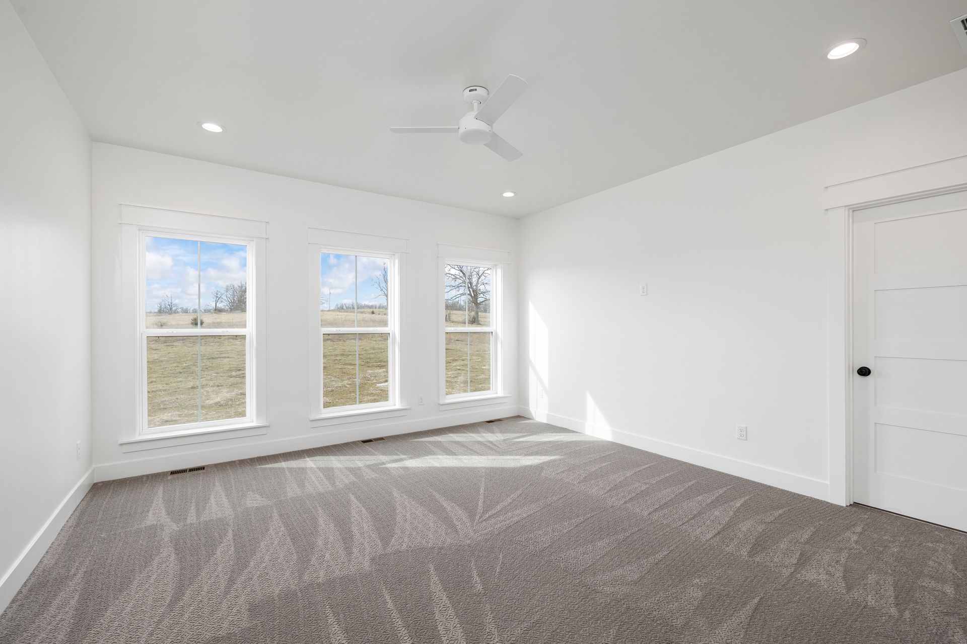 An empty bedroom with a ceiling fan and three windows.