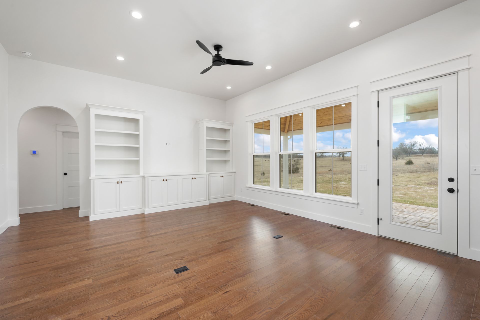 An empty living room with hardwood floors and a ceiling fan.