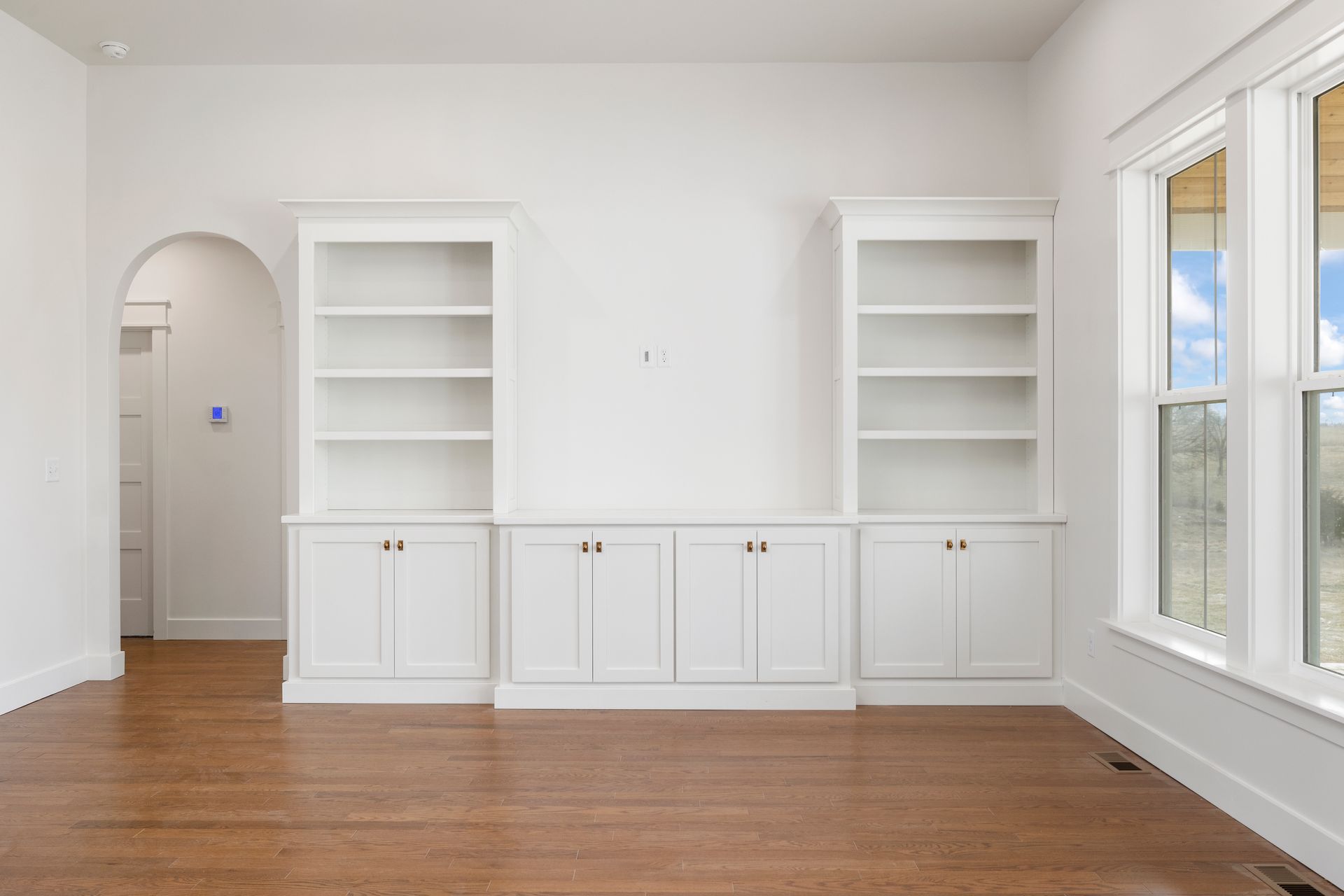 An empty living room with white cabinets and shelves and hardwood floors.