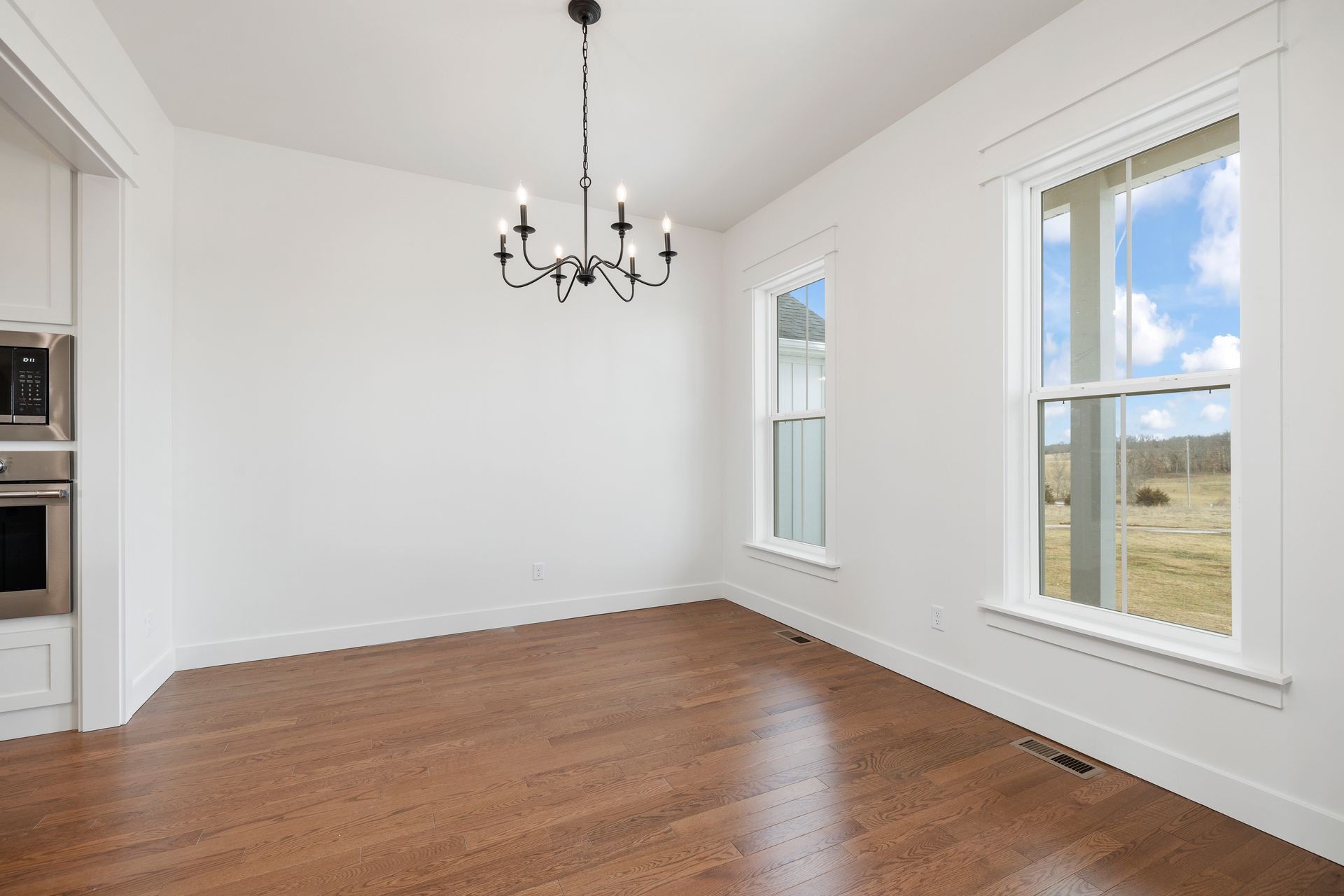 An empty dining room with hardwood floors and a chandelier hanging from the ceiling.