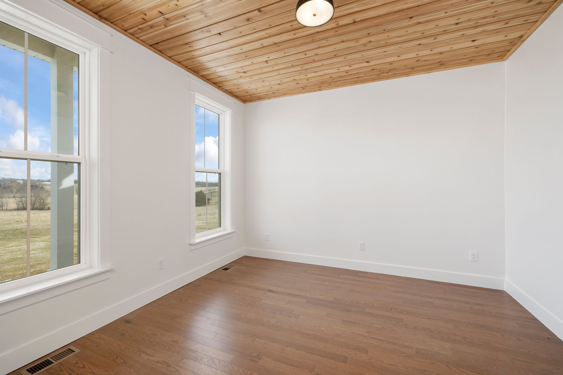 An empty room with a wooden ceiling and two windows.