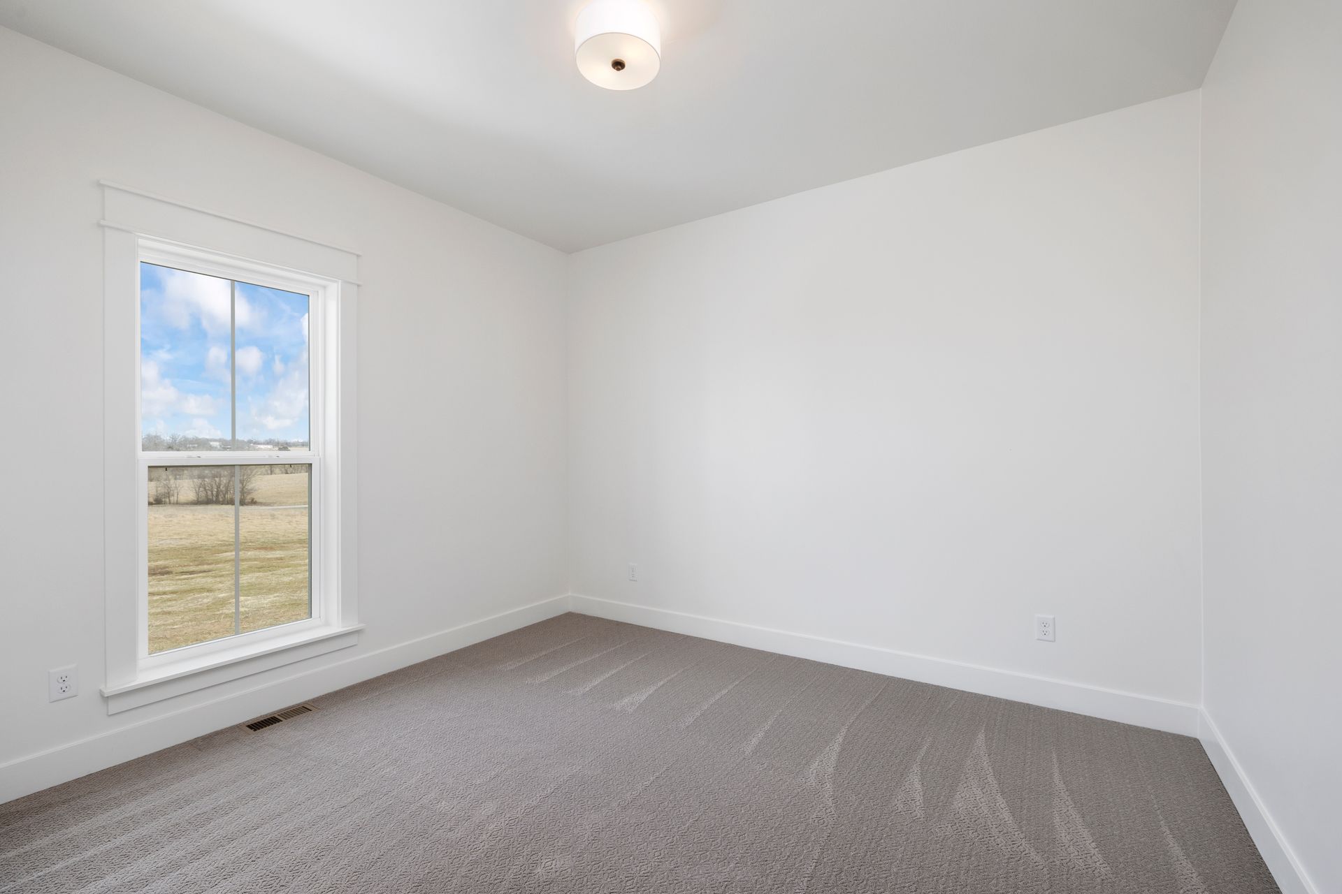 An empty bedroom with a window and a carpeted floor.