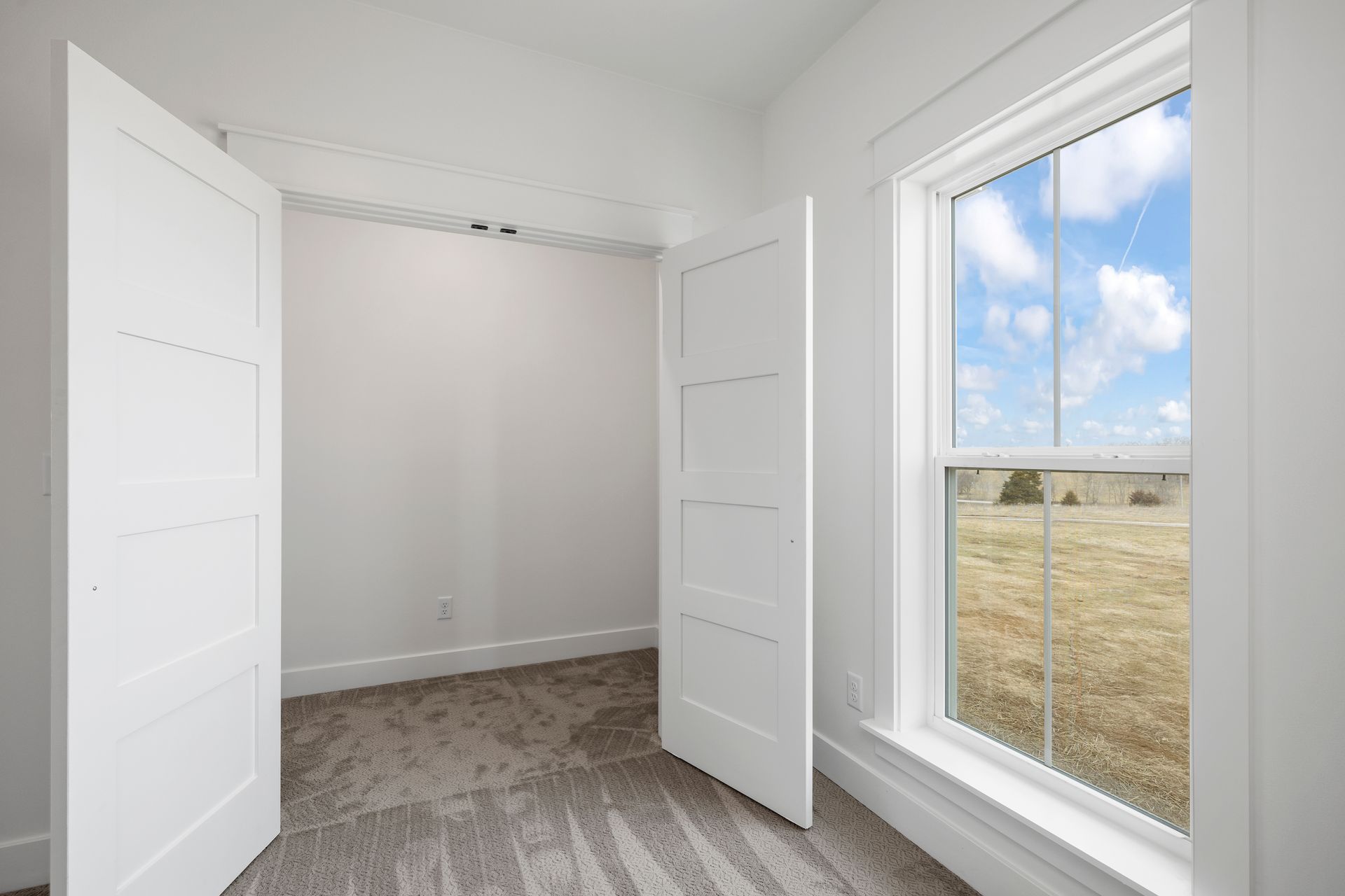 An empty bedroom with two white doors and a large window.
