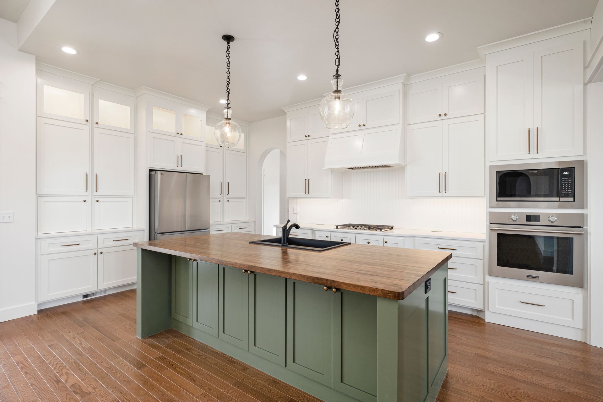 A kitchen with white cabinets , stainless steel appliances , and a green island.