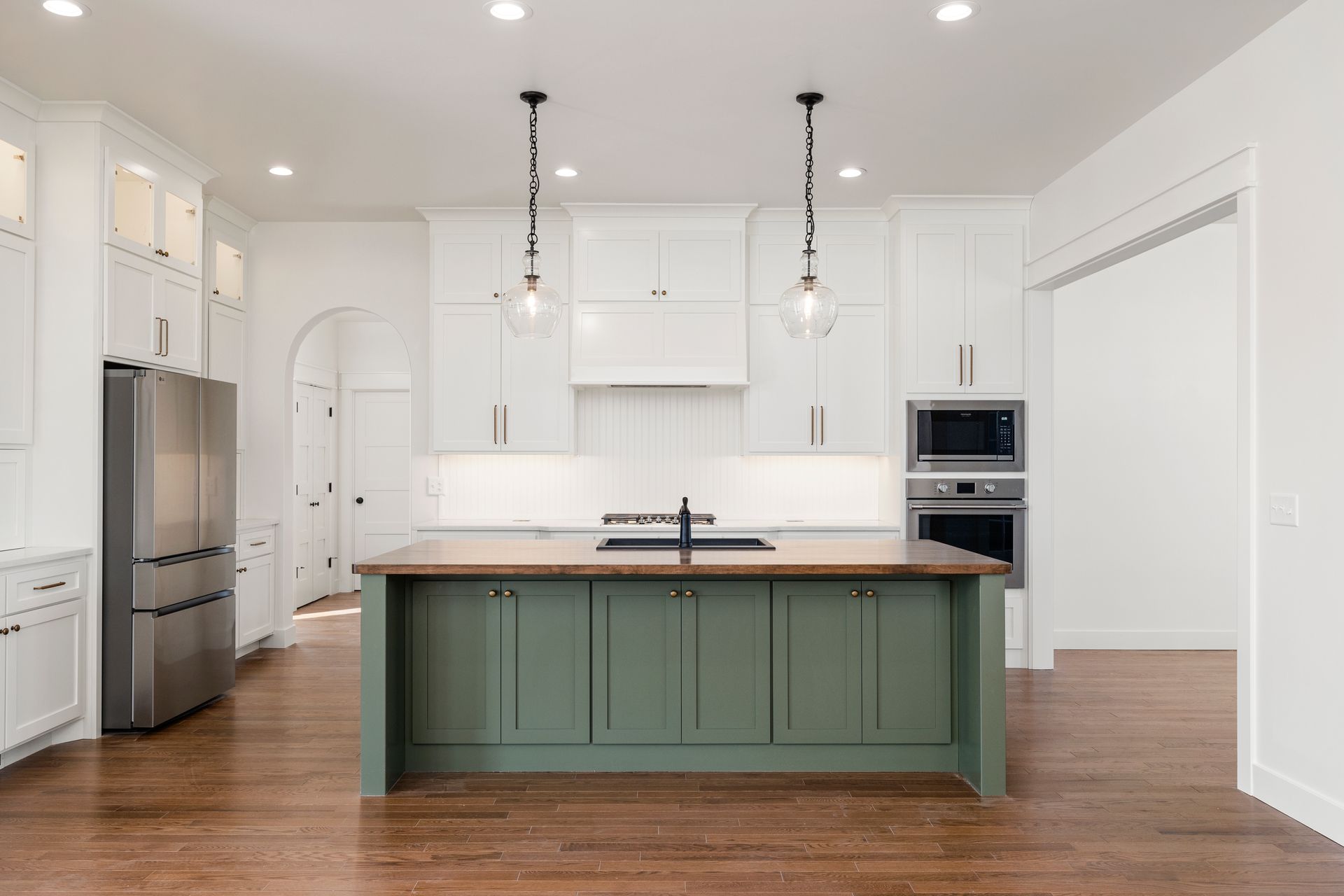 A kitchen with green cabinets , white cabinets , stainless steel appliances and a large island.