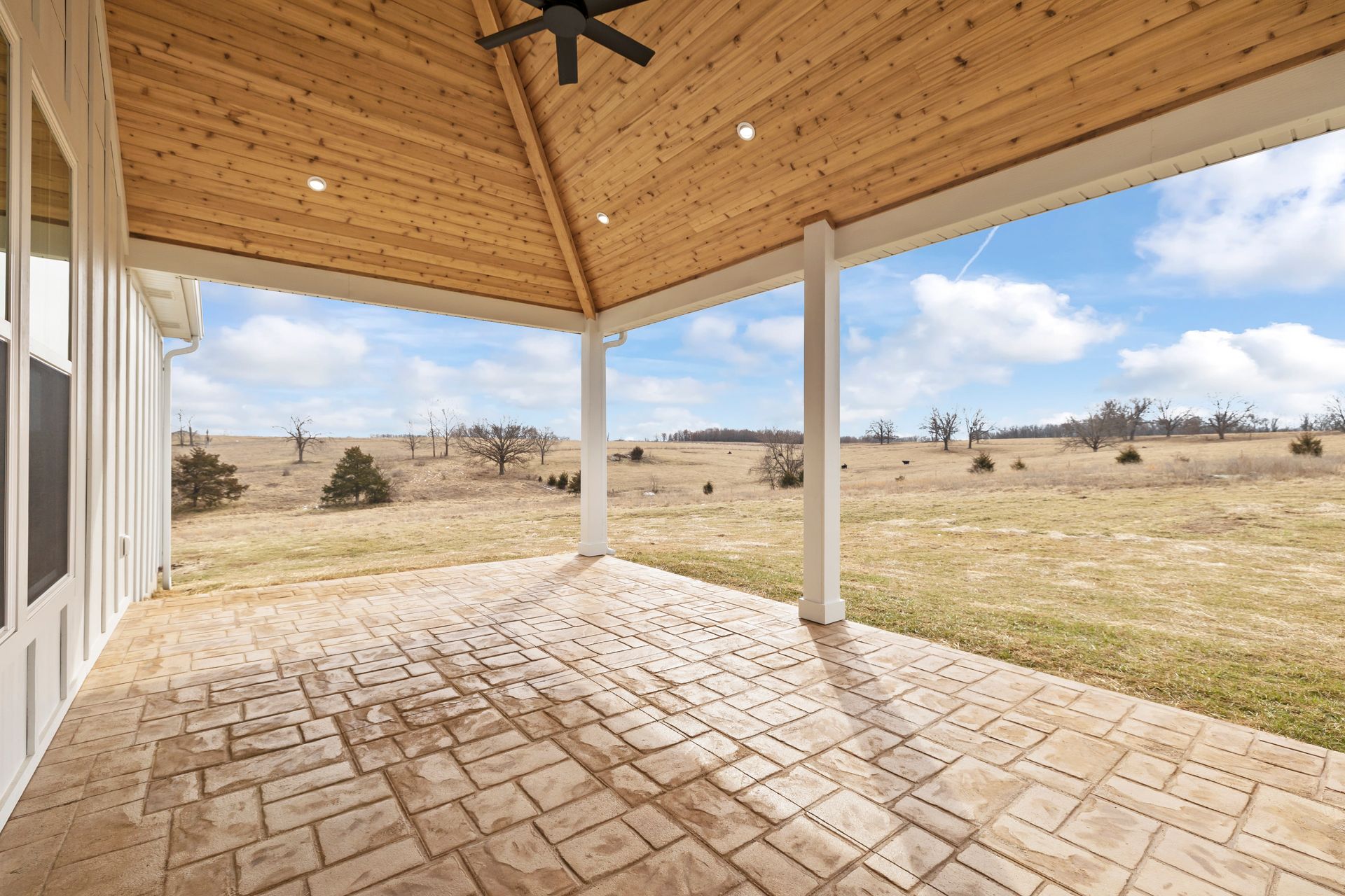 An empty porch with a ceiling fan and a view of a field.