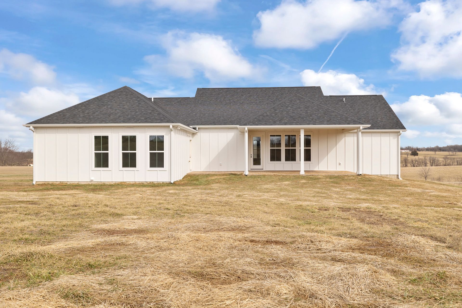 A white house with a black roof is sitting in the middle of a field.