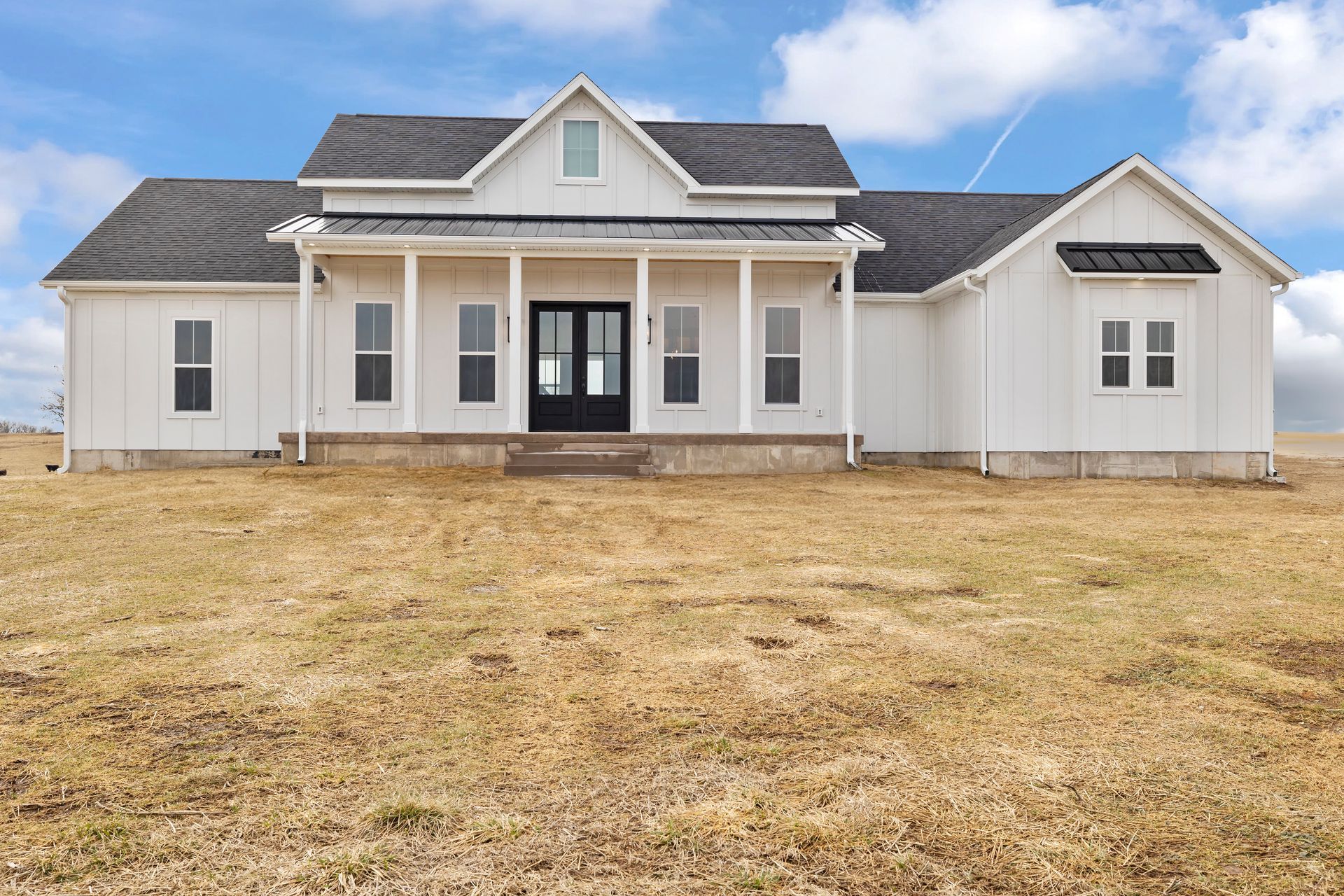A white house with black windows is sitting in the middle of a field.