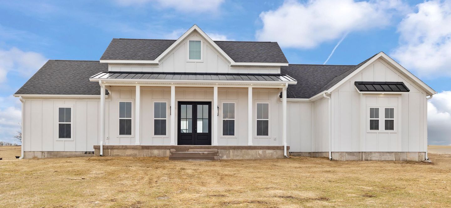 A white house with a black door is sitting in the middle of a field.