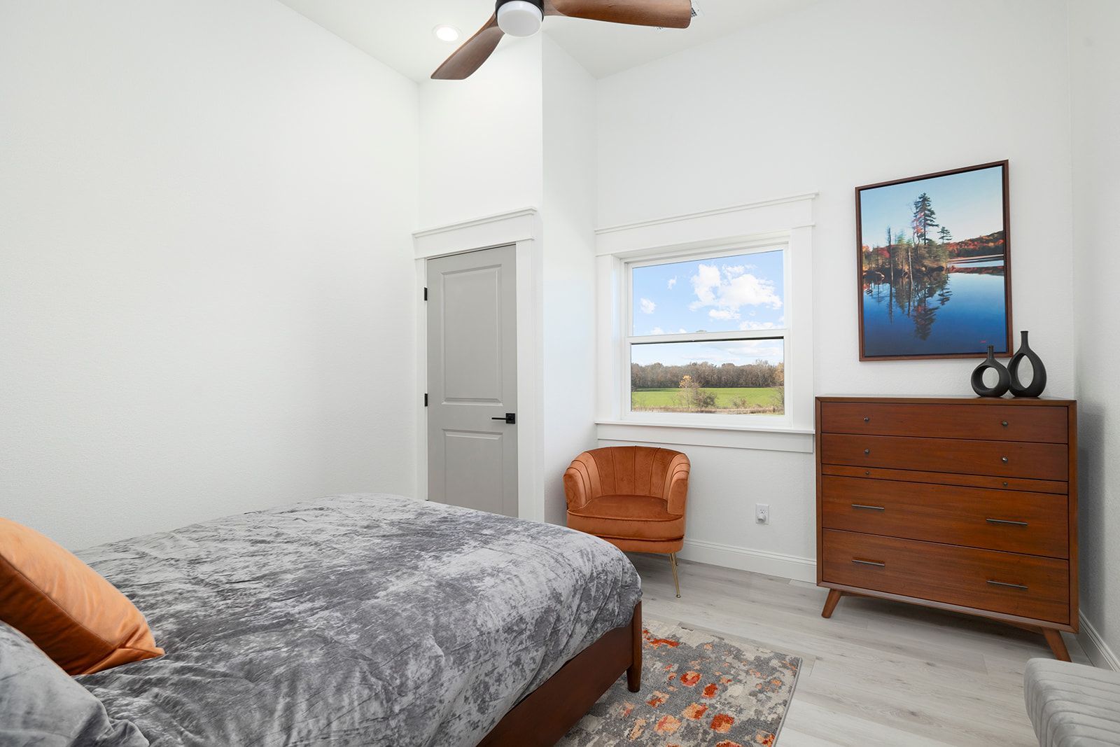 A bedroom with a bed , chair , dresser and ceiling fan.