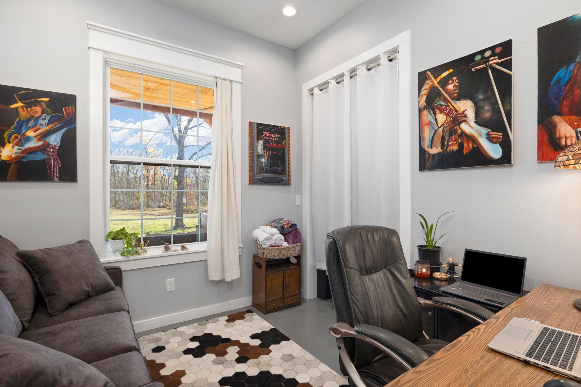 A living room with a couch , desk , chair , laptop and paintings on the wall.