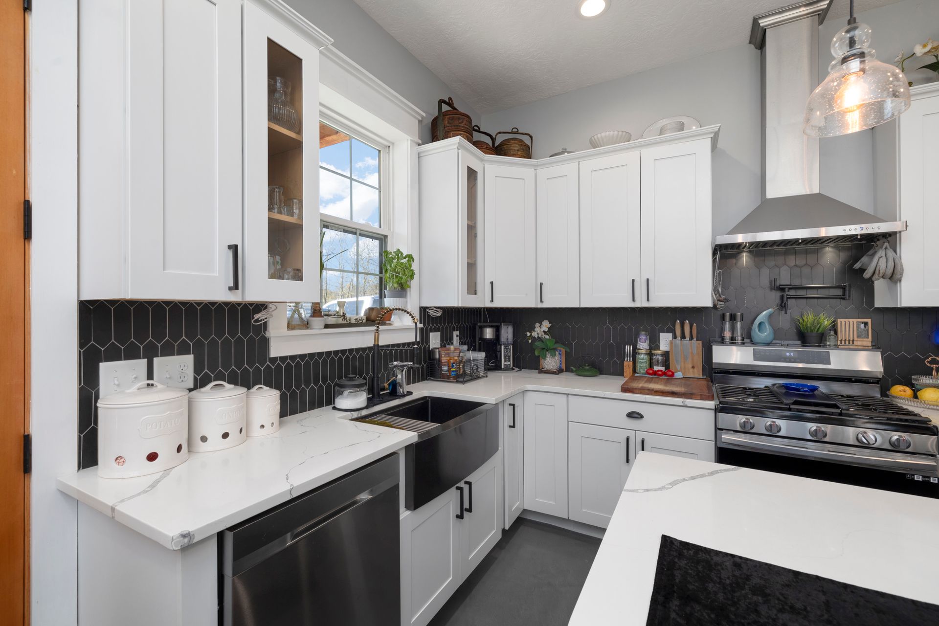 A kitchen with white cabinets , a sink , a stove , and a window.