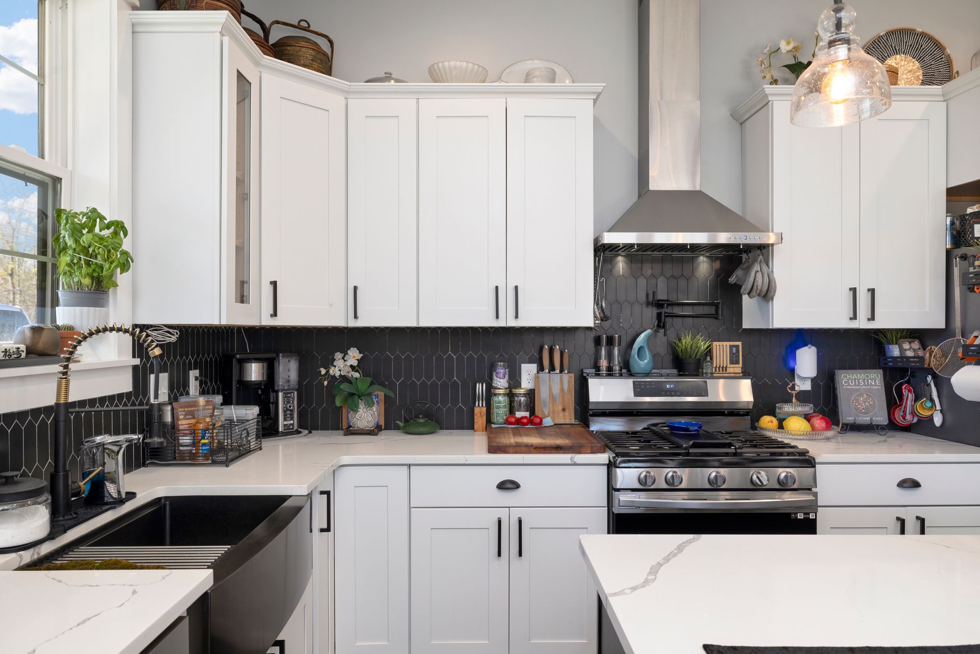 A kitchen with white cabinets , a stove , a sink , and a window.