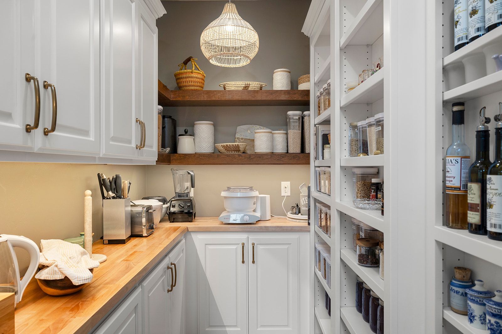 A kitchen with white cabinets and wooden counter tops and shelves filled with bottles and jars.