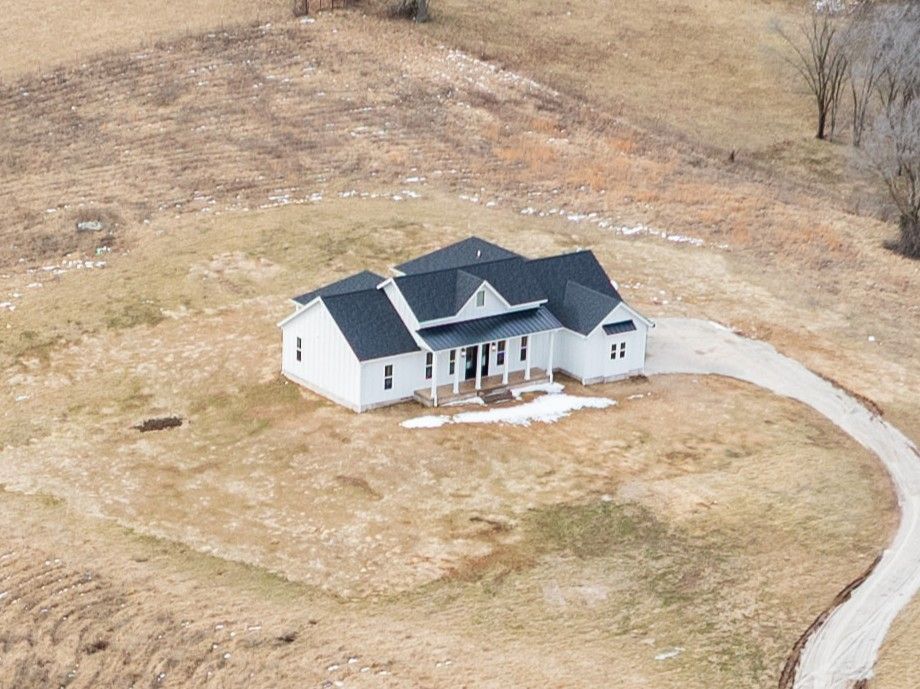 An aerial view of a white house with a black roof in the middle of a field.