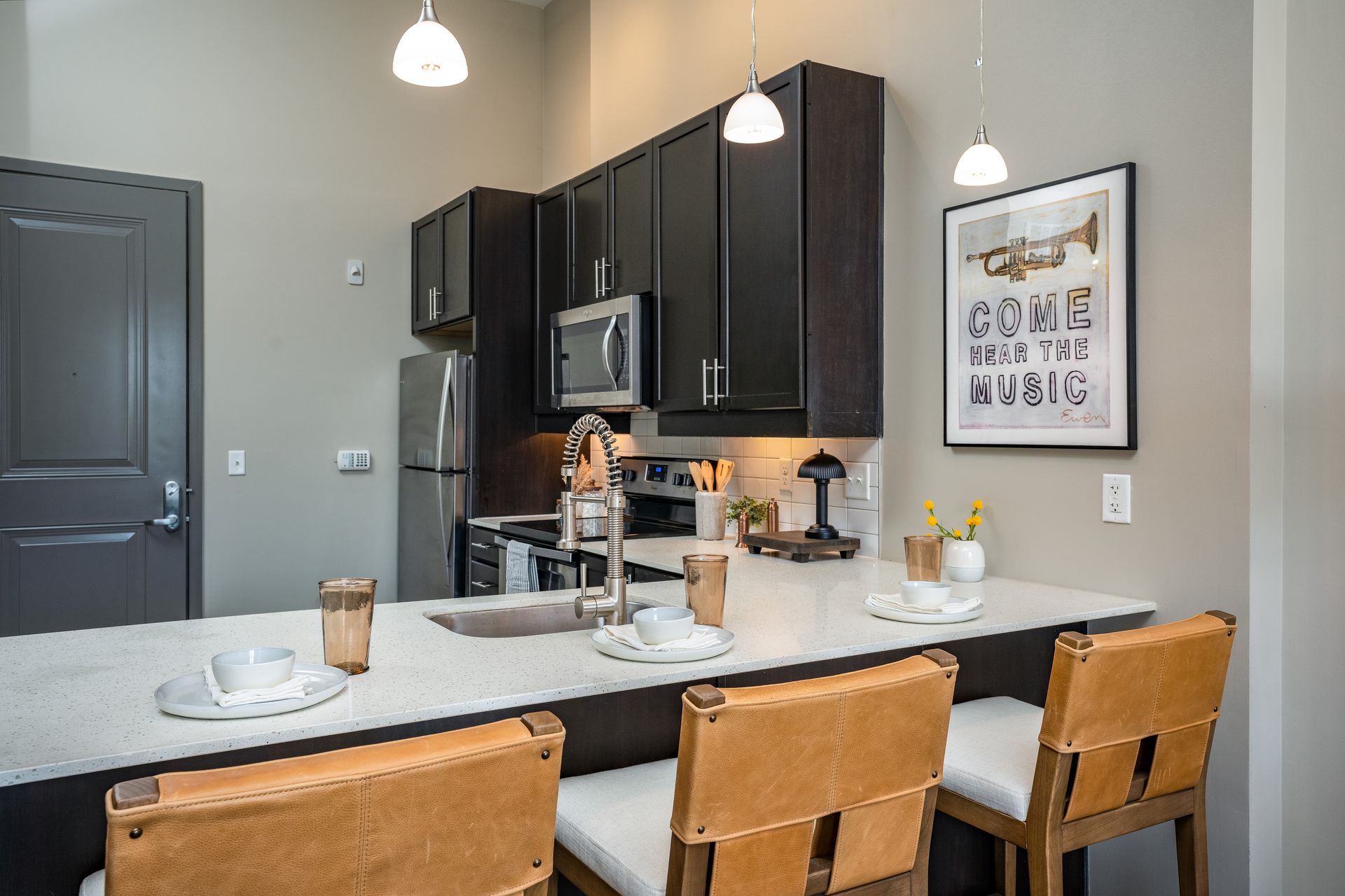 A modern kitchen with dark cabinets, stainless steel appliances, a breakfast bar with stools, and a framed musical print.