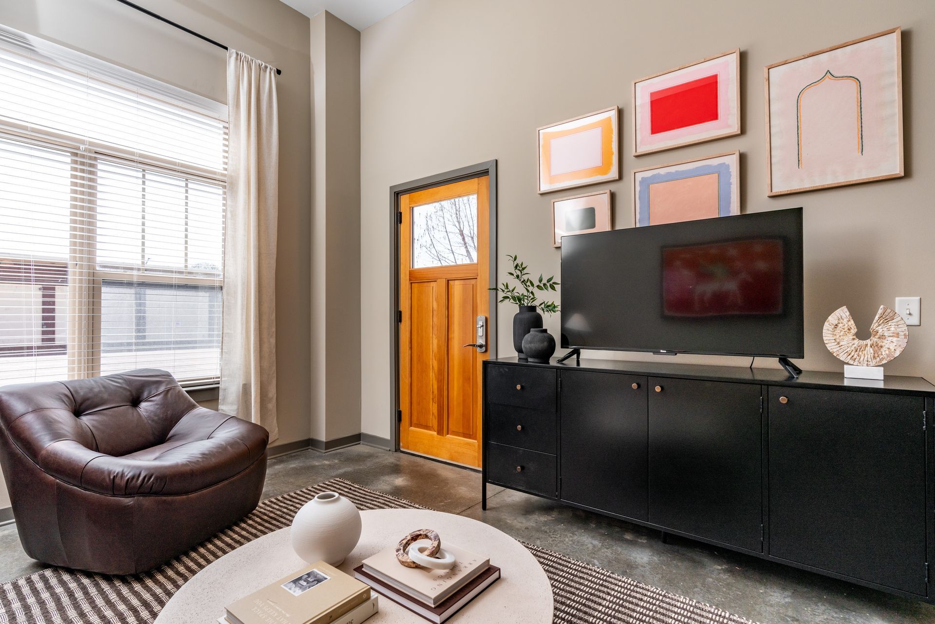 A living room with a chair , coffee table , television and paintings on the wall.
