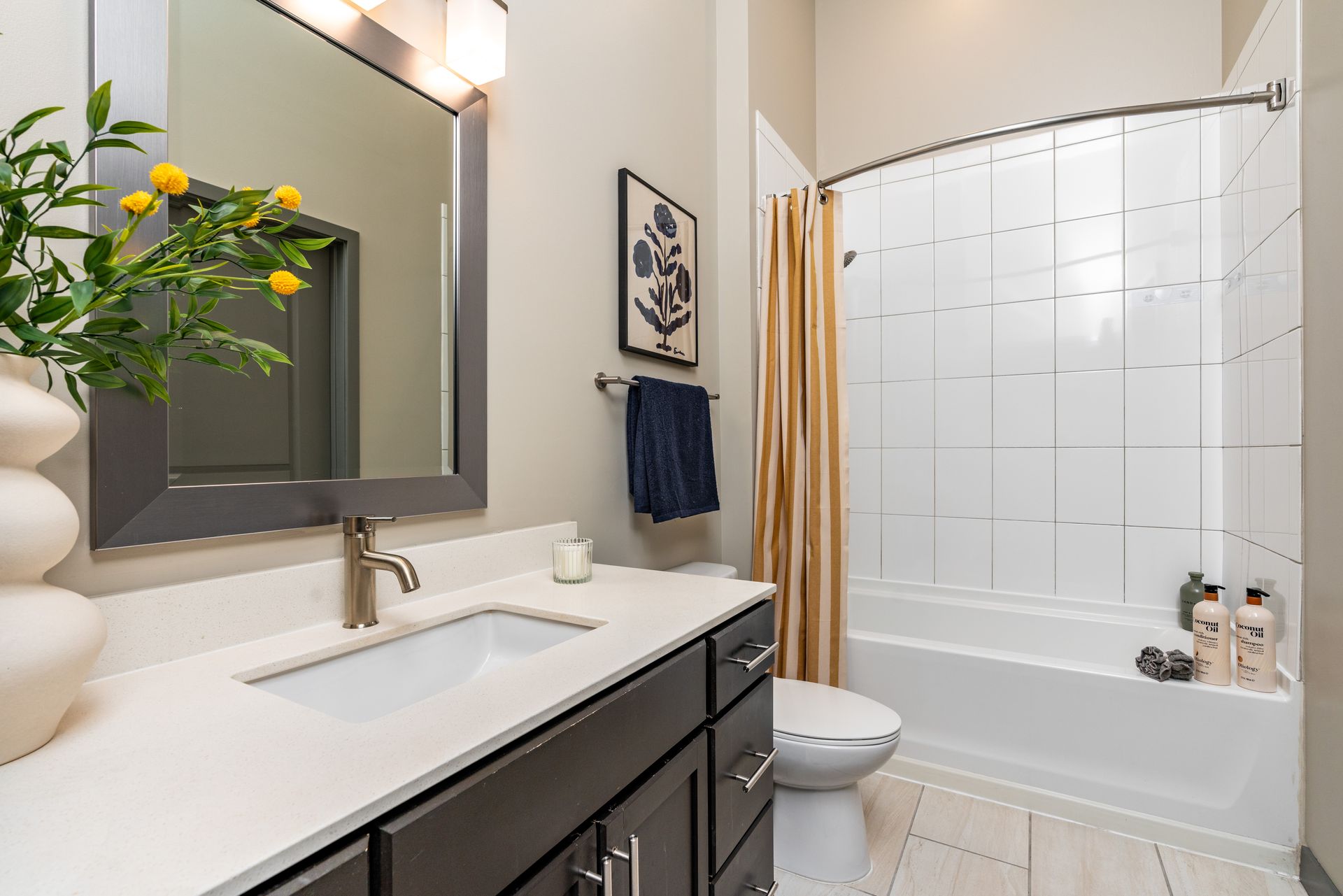 Bathroom with a white sink, dark cabinets, beige walls, and a shower with a striped curtain.