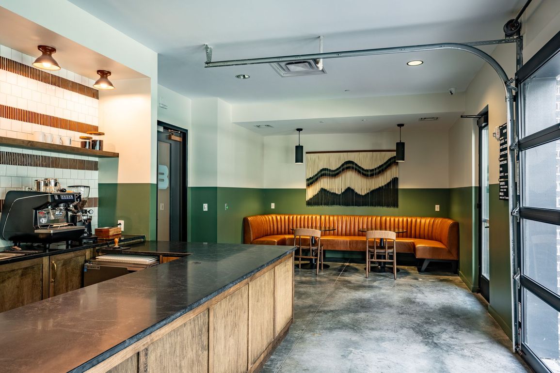 Interior of a coffee shop with a counter, seating area, and an open garage door. 