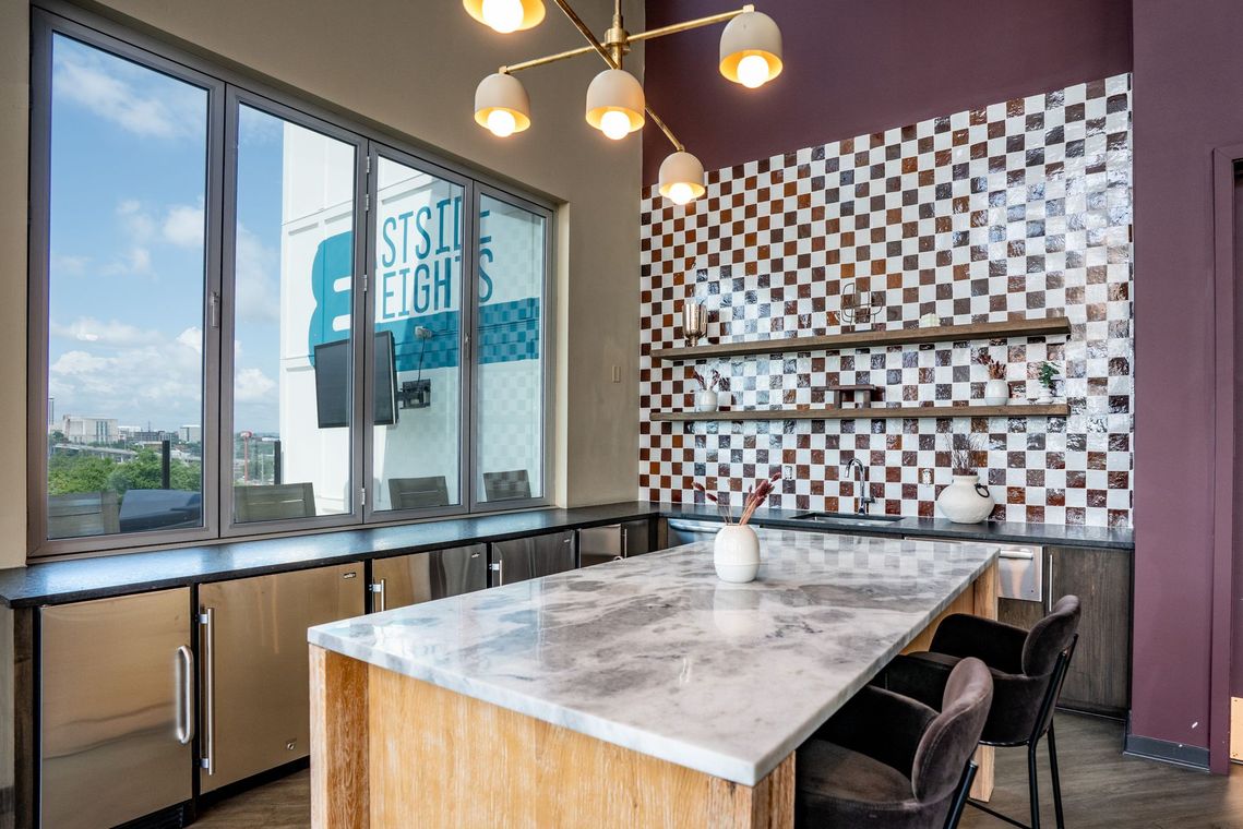Modern kitchen and dining area with marble island, checkered backsplash, and a view of a city skyline.