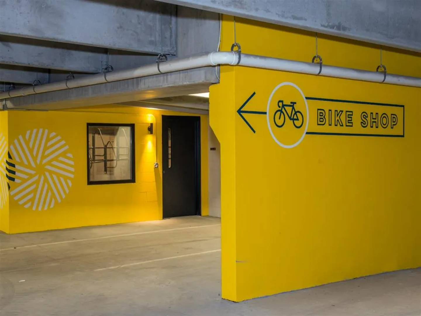 Yellow painted walls in a parking garage direct to a bike shop. Signage includes a bicycle symbol and directional arrow.