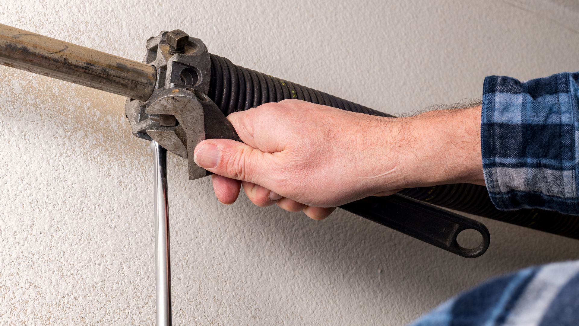 Hand using a wrench to adjust a garage door torsion spring assembly.