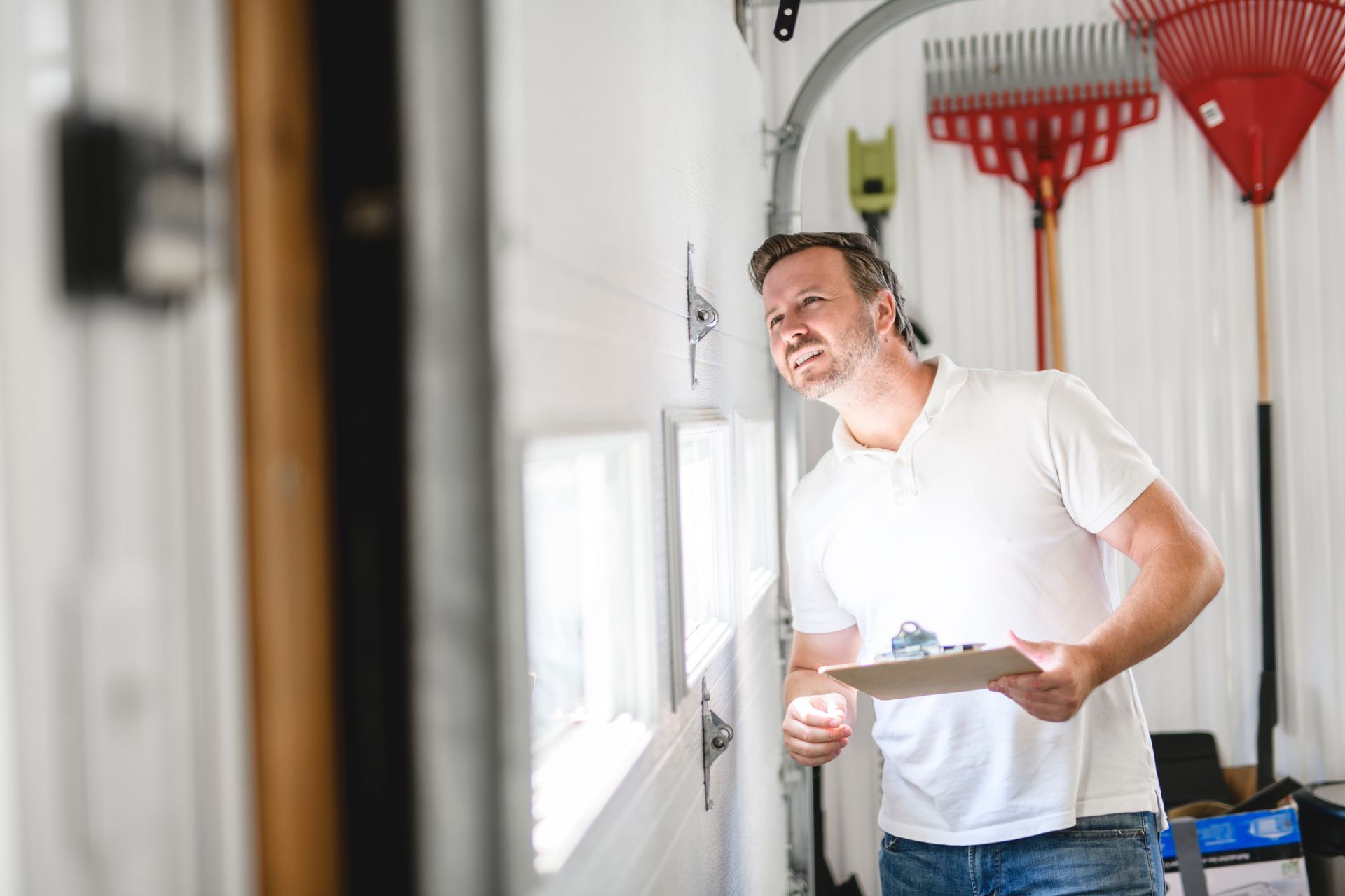 Person inspecting a garage door while holding a clipboard inside a residential garage. Person inspecting a garage door while holding a clipboard inside a residential garage.