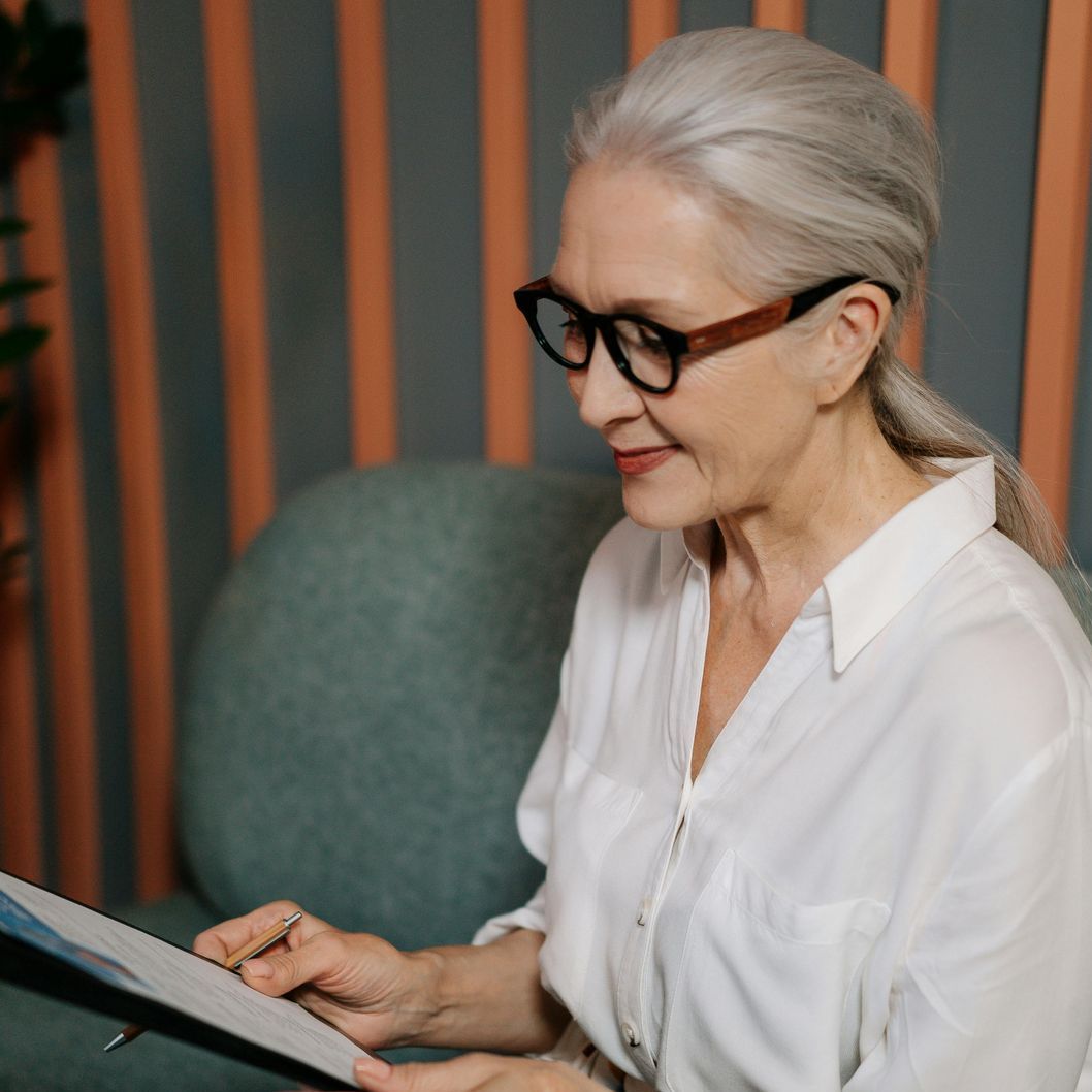 An older woman wearing glasses is sitting in a chair reading a book.