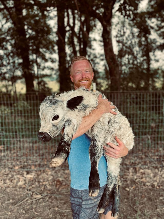 A man is holding a baby cow in his arms.