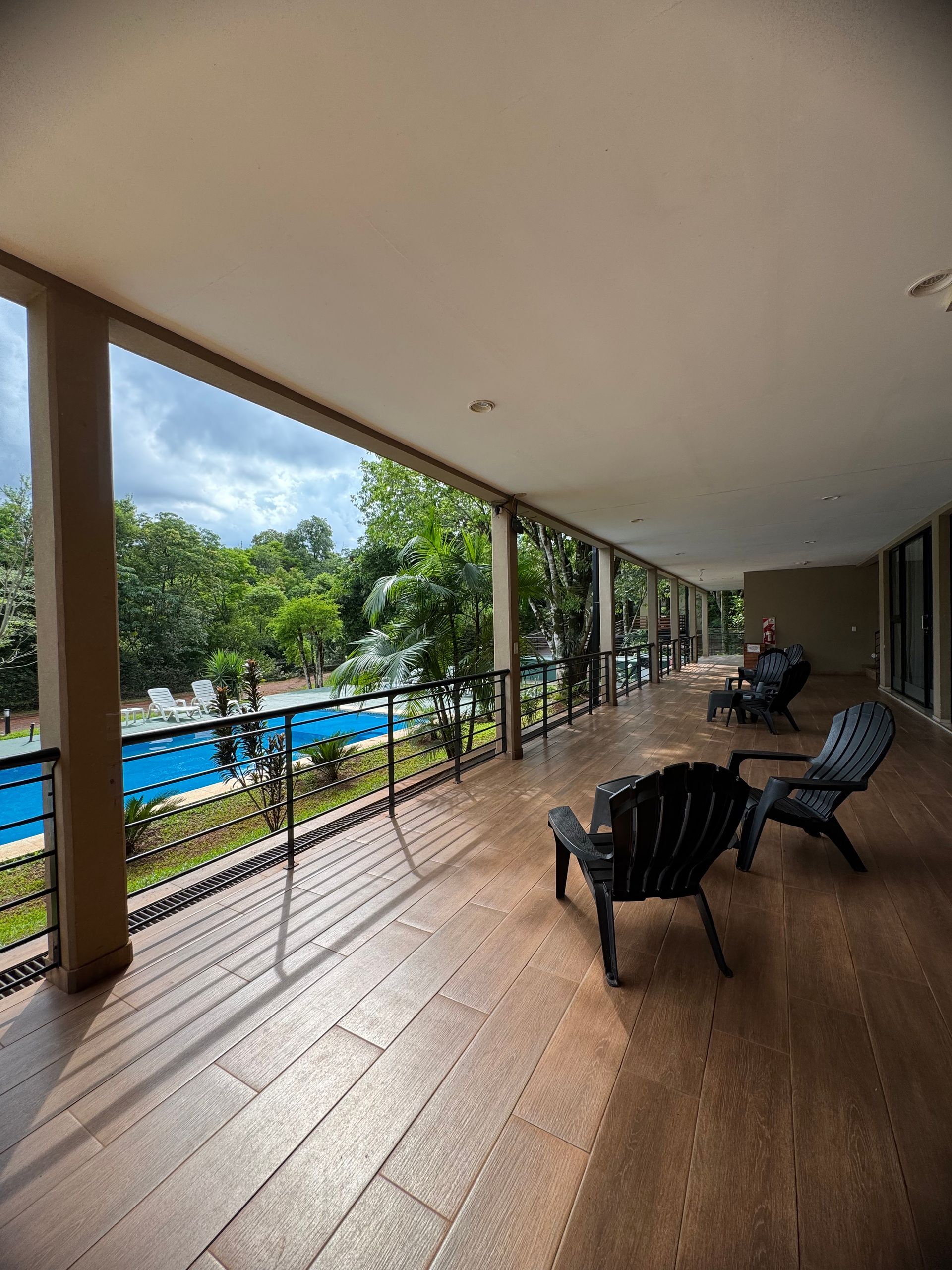 A balcony with chairs and a table overlooking a swimming pool.