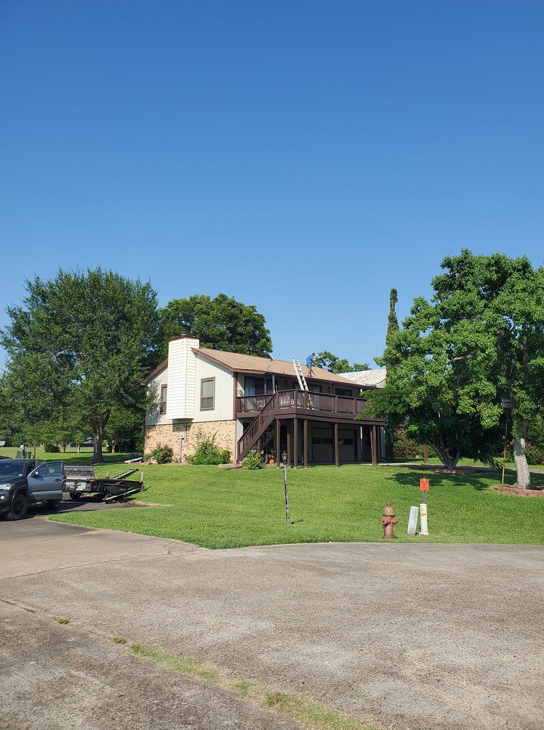 Rustic house with porch on a grassy lot under a clear blue sky, seen from a gravel driveway