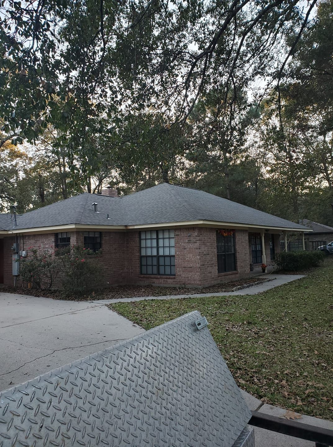 Brick house with a gray roof and trees in the yard, seen from a driveway with a truck bed in the foreground