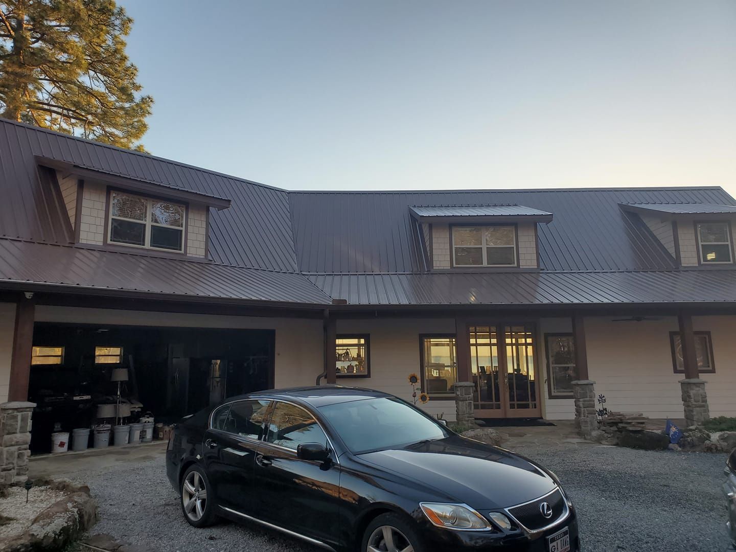 Black sedan parked in front of a large house with dormer windows at dusk