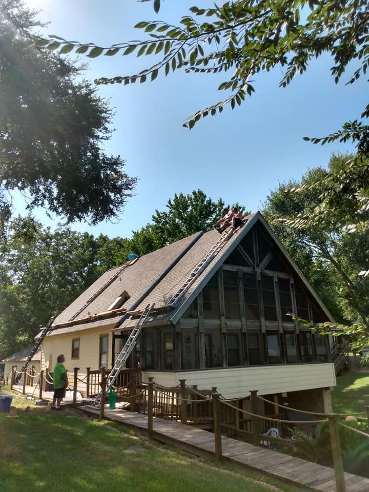 A modern A-frame cabin with a steep roof and large windows, surrounded by trees and a grassy yard.