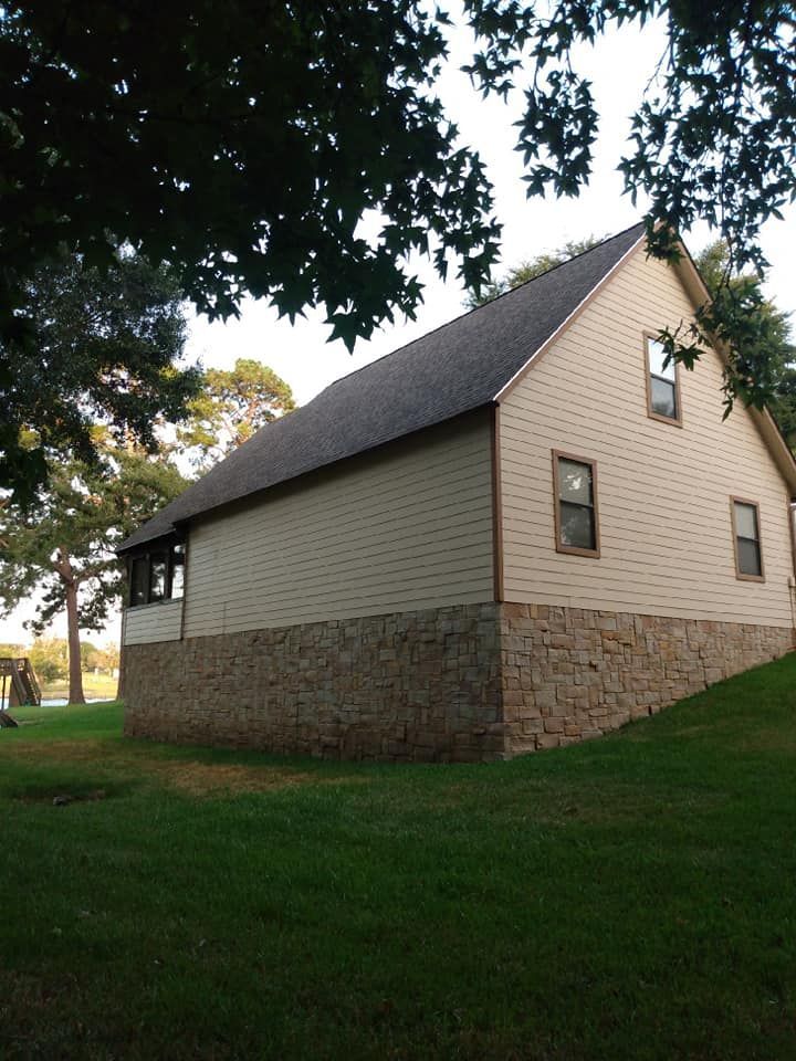 Stone-and-beige church building with a steep roof, viewed from the side beneath tree branches.