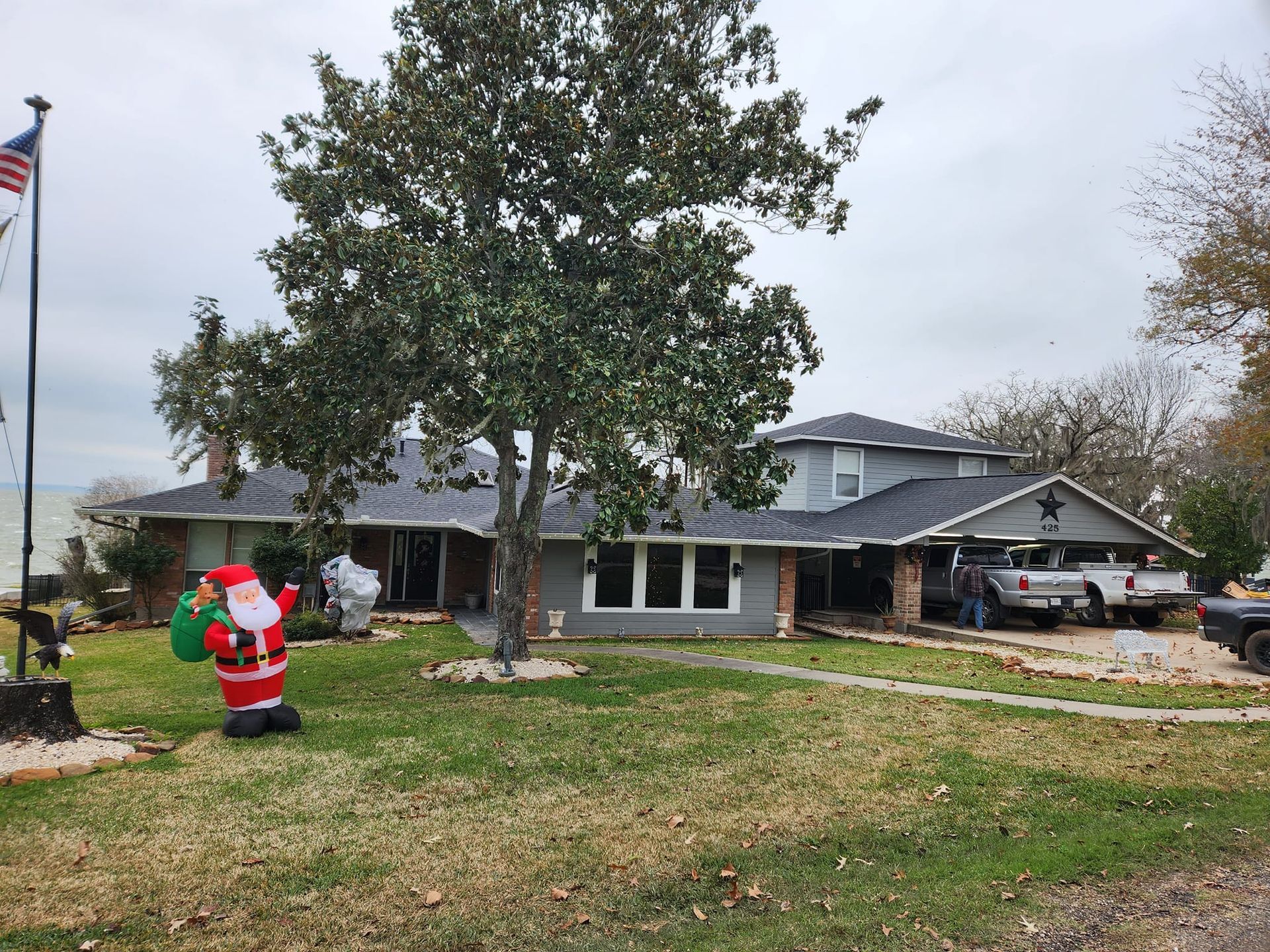 Santa Claus lawn decoration in front of a suburban house with a large tree and parked truck