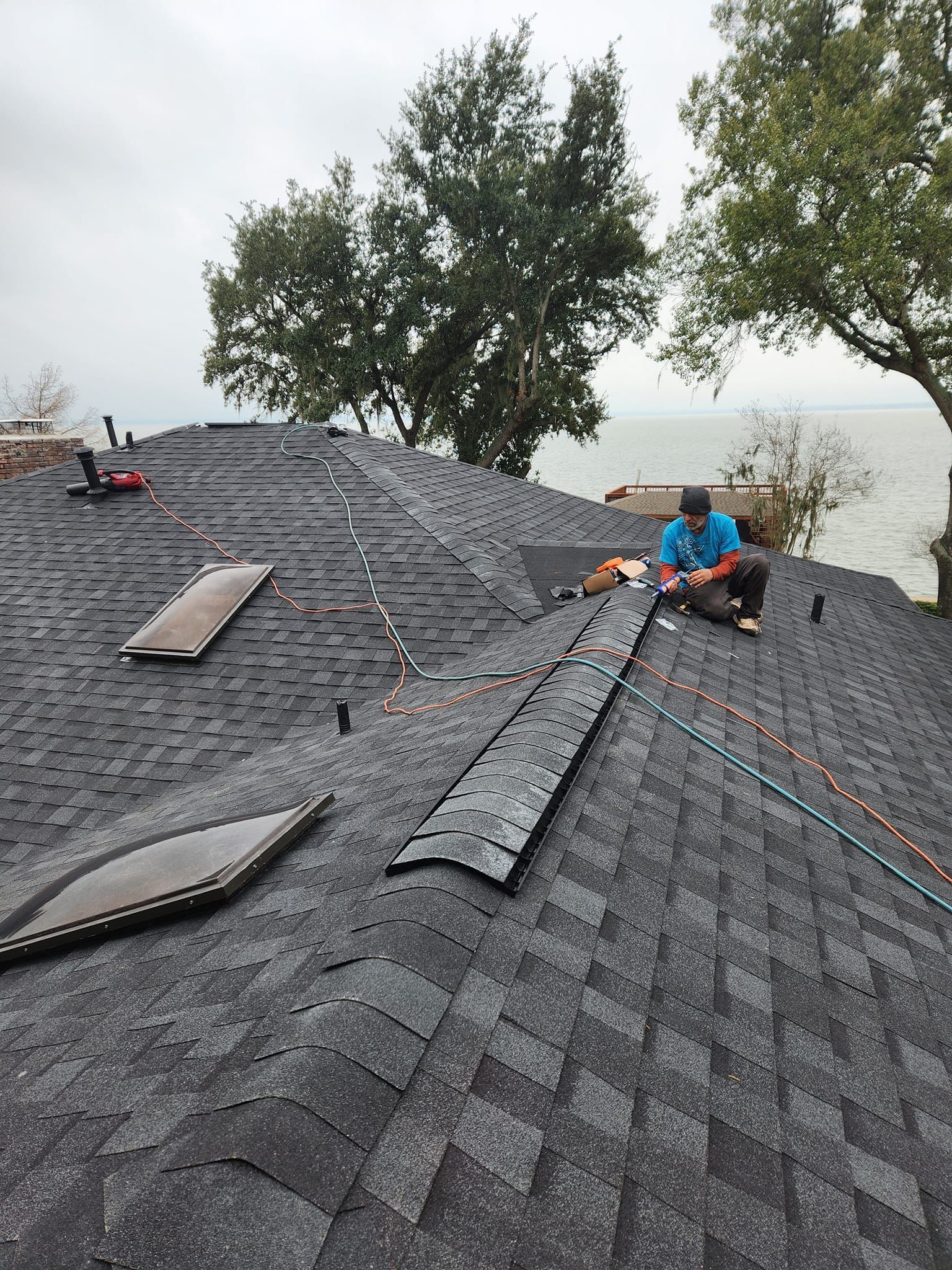 Workers repairing shingles on a steep gray roof near trees and fog