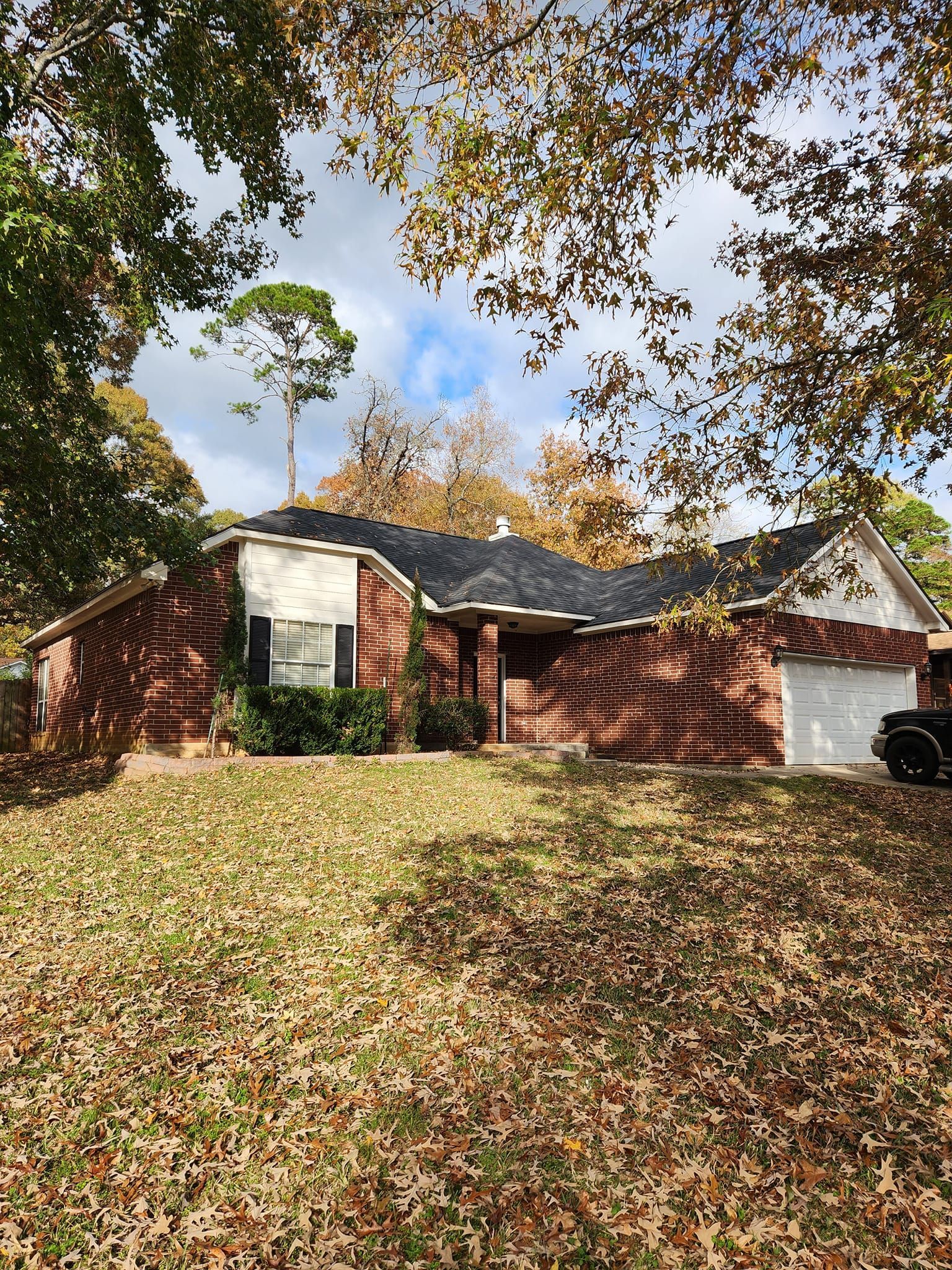 Suburban brick house with white shutters and garage, surrounded by autumn leaves and trees